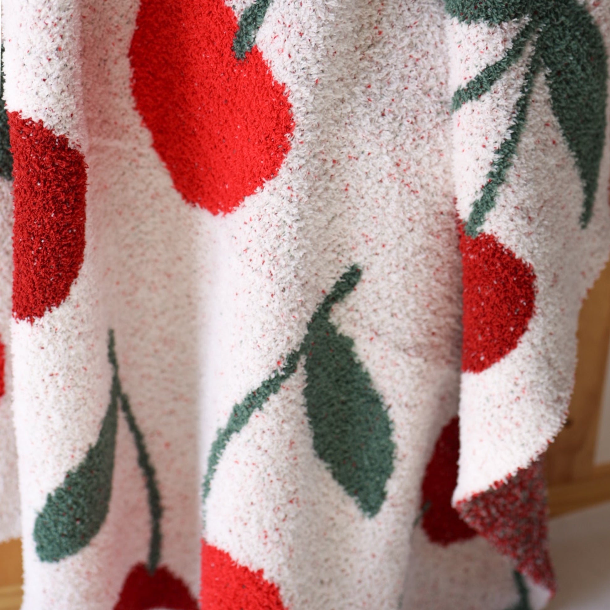 Close-up of the Plush Blanket | Cherry by forever french baby, an OEKO-TEX certified microfiber blanket with a fluffy texture and vibrant red cherry and green leaf pattern on a white background.