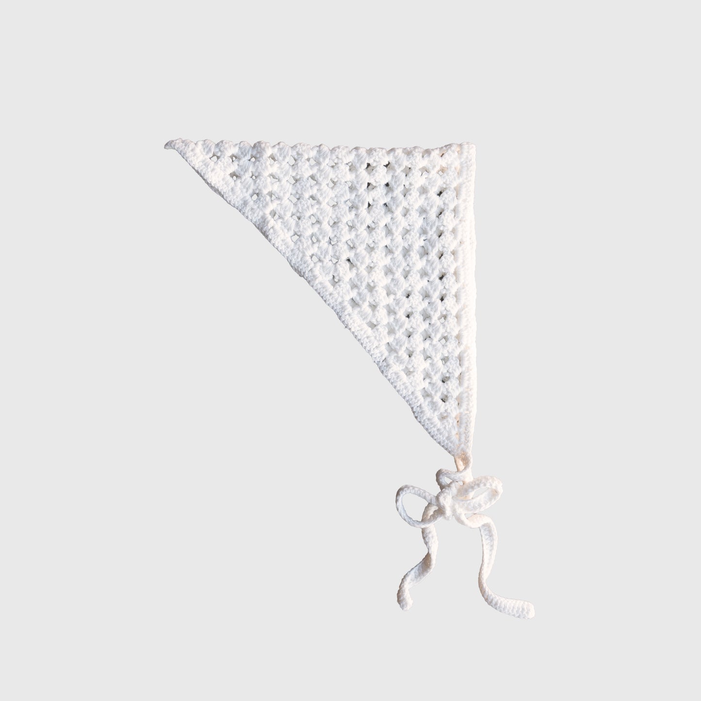 The Knit Head Scarf | Cloud by forever french baby is a white, hand-crocheted triangular bandana made from soft cotton yarn. It features a delicate lacy pattern and two long, adjustable ties at the bottom, and is displayed against a plain light gray background.
