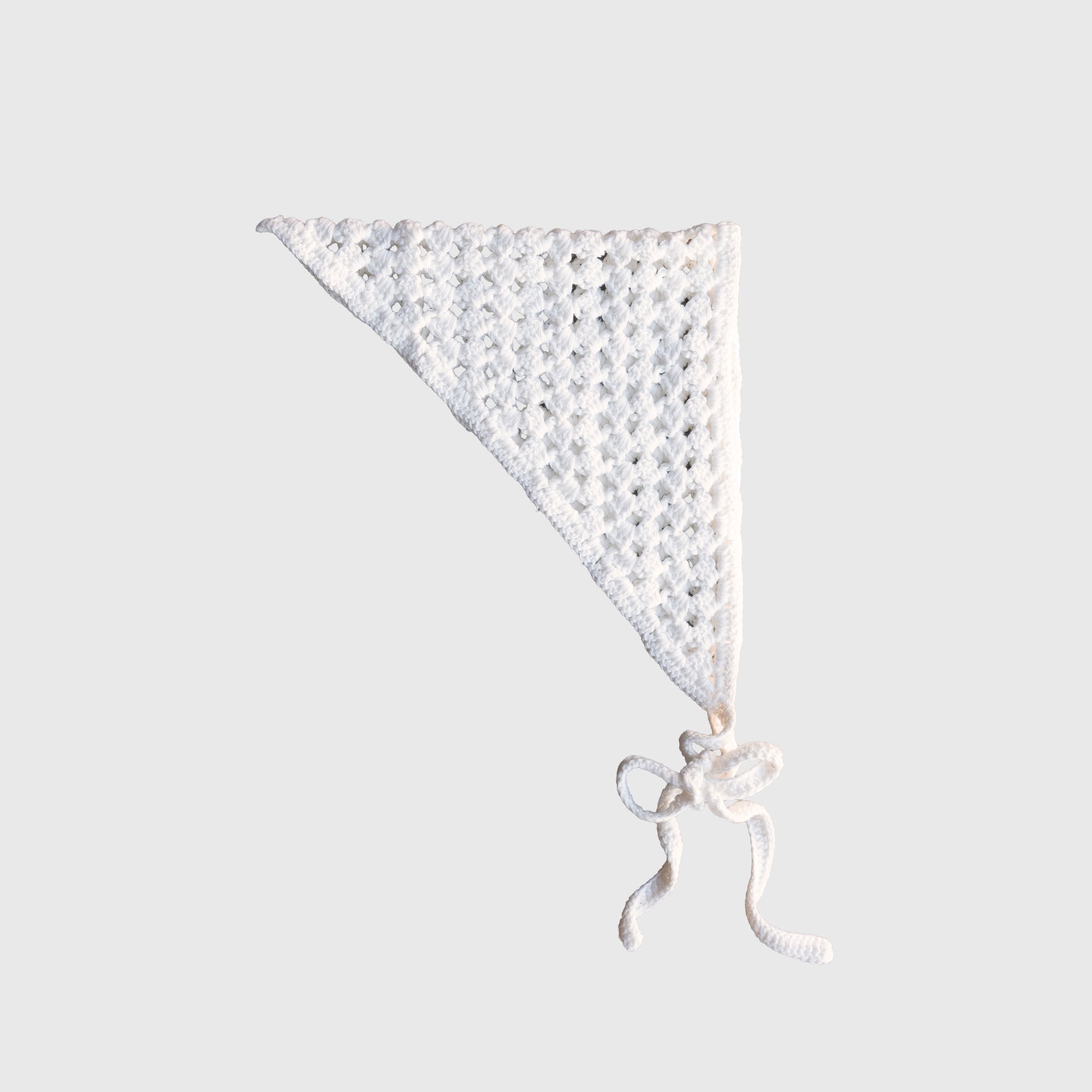 The Knit Head Scarf | Cloud by forever french baby is a white, hand-crocheted triangular bandana made from soft cotton yarn. It features a delicate lacy pattern and two long, adjustable ties at the bottom, and is displayed against a plain light gray background.