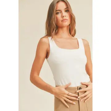 A person with long, wavy hair stands against a neutral background, wearing the Double Layered Square Neck Tank Top in off white by forever french baby. They pair the soft rayon fabric top with high-waisted, light brown pants. Their hands rest near their waist as they pose confidently.