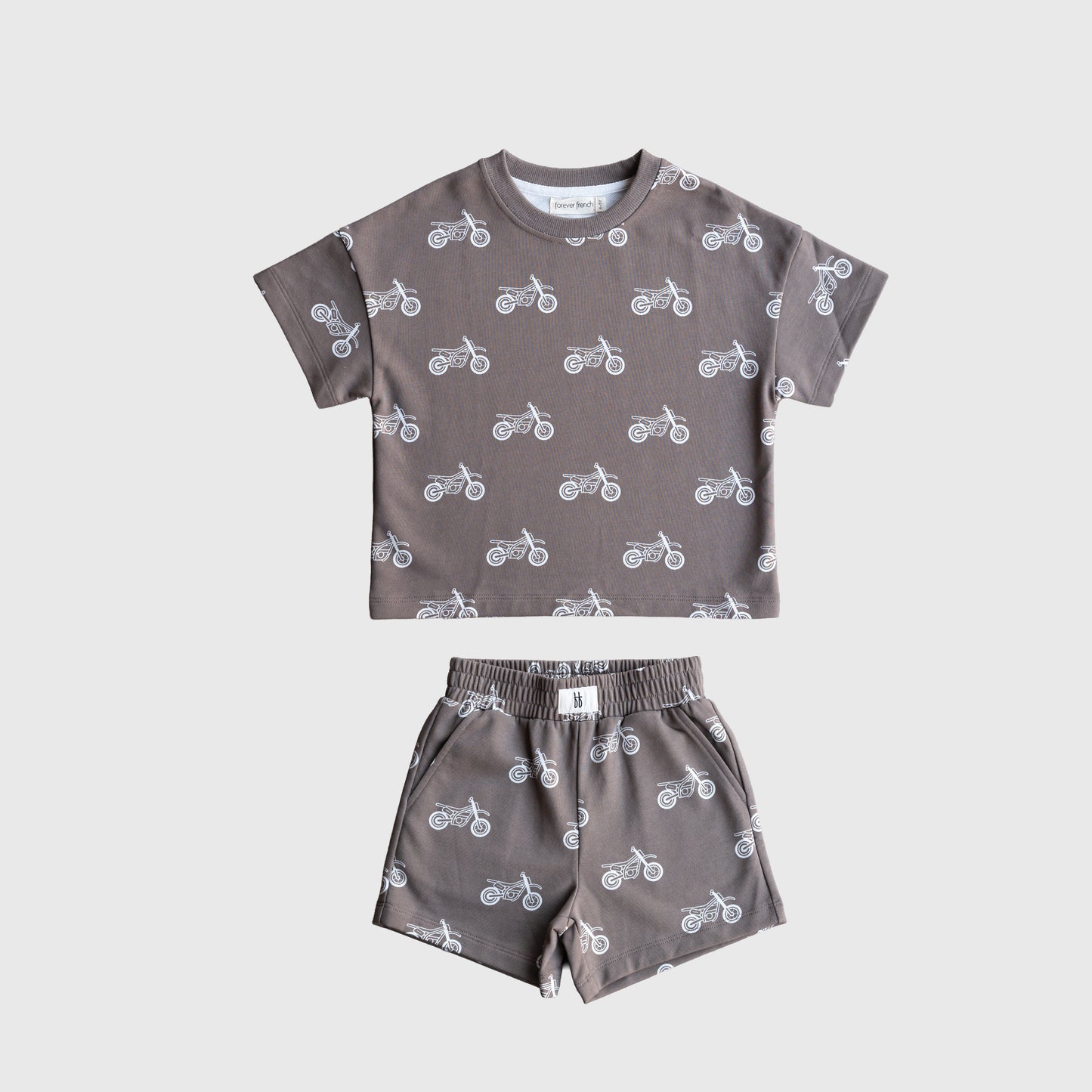 The forever french baby French Terry Short Set | Dirt Bike is a gray kids’ matching set with a short sleeve top and elastic waistband shorts, both featuring a white dirt bike pattern, displayed flat on a plain white background.