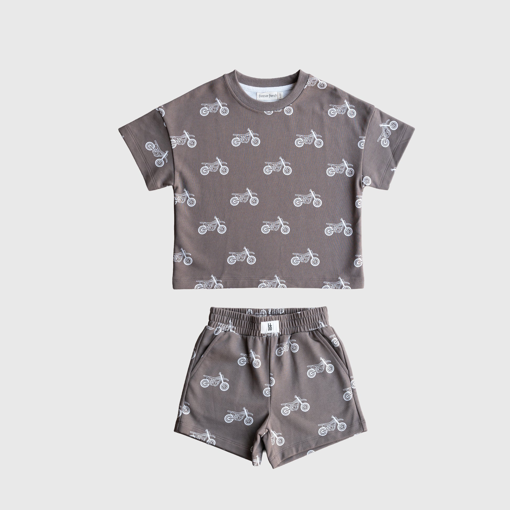 The forever french baby French Terry Short Set | Dirt Bike is a gray kids’ matching set with a short sleeve top and elastic waistband shorts, both featuring a white dirt bike pattern, displayed flat on a plain white background.