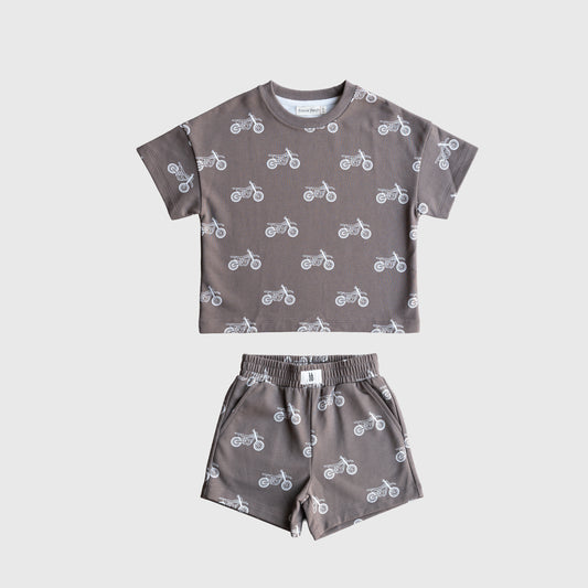 The forever french baby French Terry Short Set | Dirt Bike is a gray kids’ matching set with a short sleeve top and elastic waistband shorts, both featuring a white dirt bike pattern, displayed flat on a plain white background.