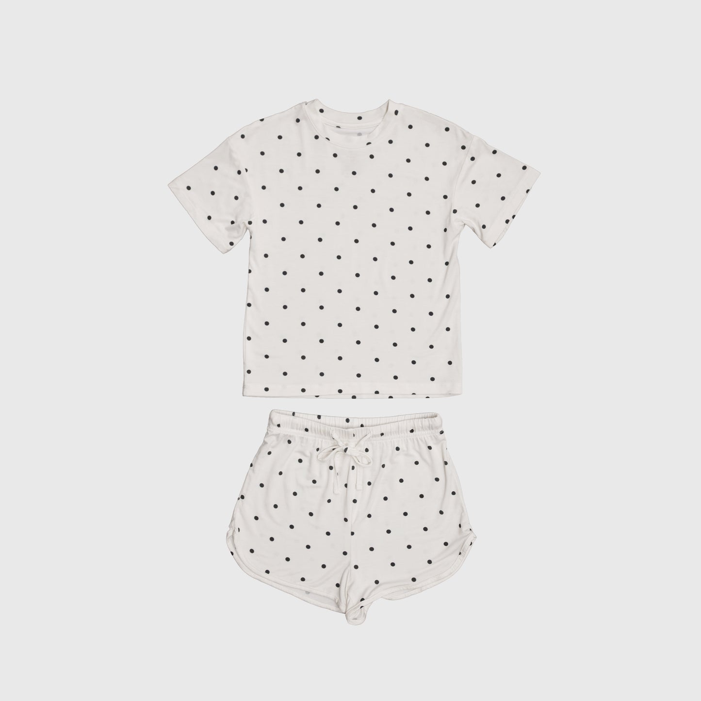 The Girl's Bamboo Short Set | Annie by forever french baby includes a white short-sleeve tee and drawstring shorts with black polka dots, made from breathable bamboo for comfort on warm nights. Displayed on a plain light background.