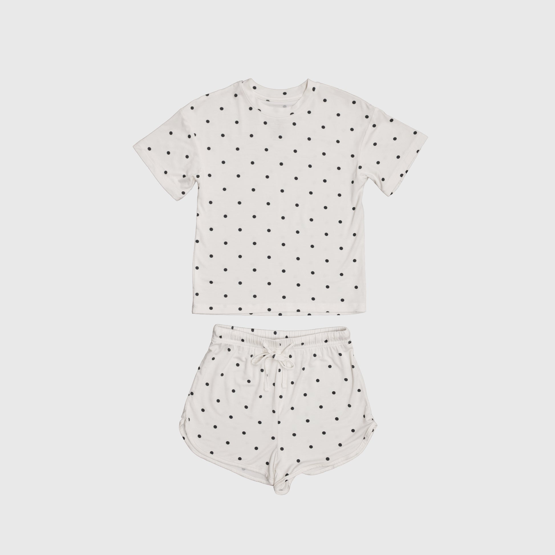 The Girl's Bamboo Short Set | Annie by forever french baby includes a white short-sleeve tee and drawstring shorts with black polka dots, made from breathable bamboo for comfort on warm nights. Displayed on a plain light background.