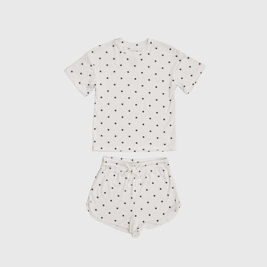 The Girl's Bamboo Short Set | Annie by forever french baby includes a white short-sleeve tee and drawstring shorts with black polka dots, made from breathable bamboo for comfort on warm nights. Displayed on a plain light background.