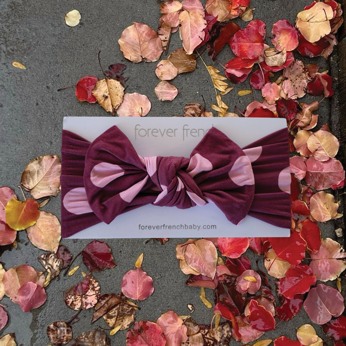 A “Bamboo Head Wrap | Heather Rose Dot” by forever french baby rests on a branded card, placed on a wet surface with scattered red and pink autumn leaves.