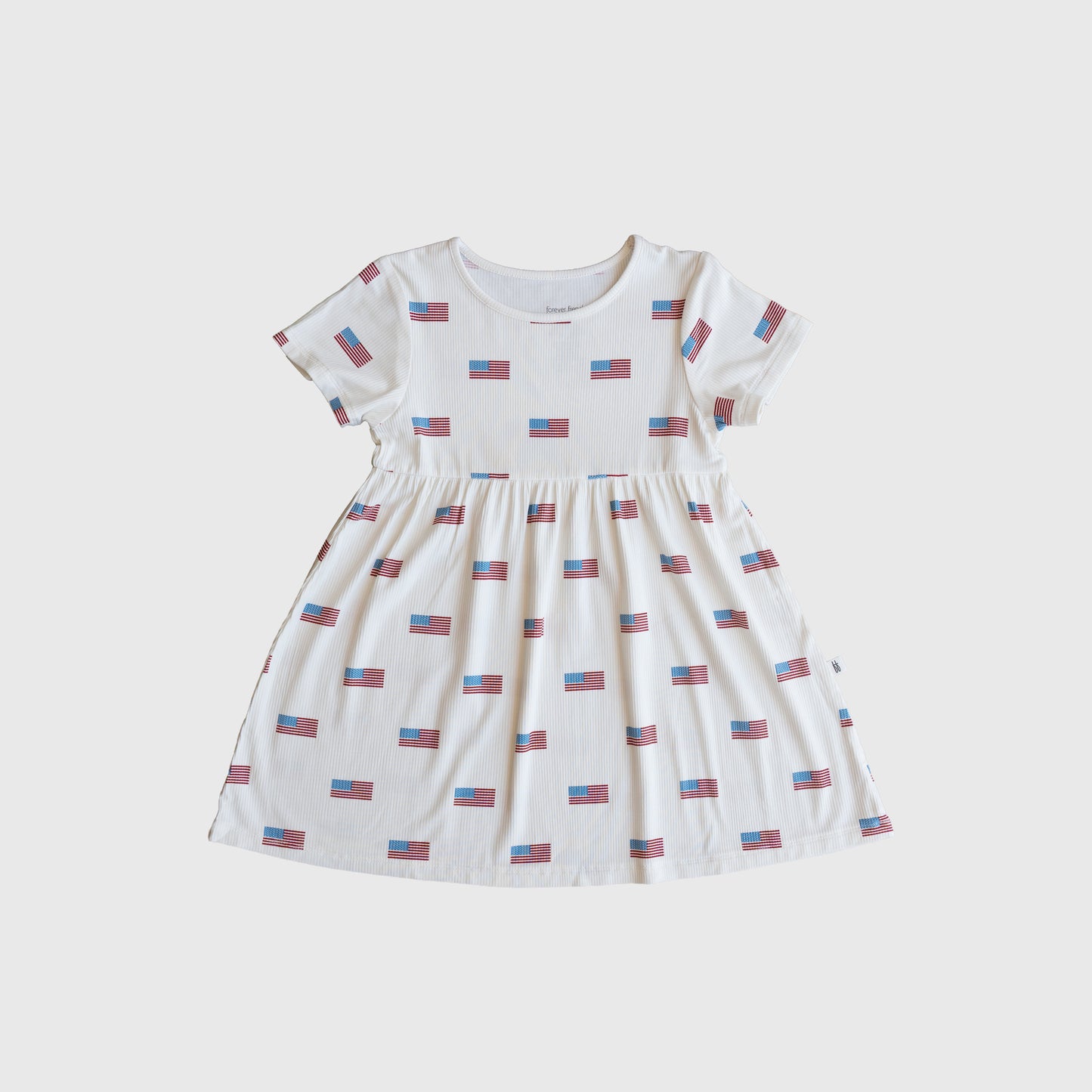 The forever french baby Bamboo T-Shirt Dress | Americana Ribbed is a hypo-allergenic, short-sleeved white children’s dress with a round neck, gathered waist, and small American flag print for softness and patriotic style.