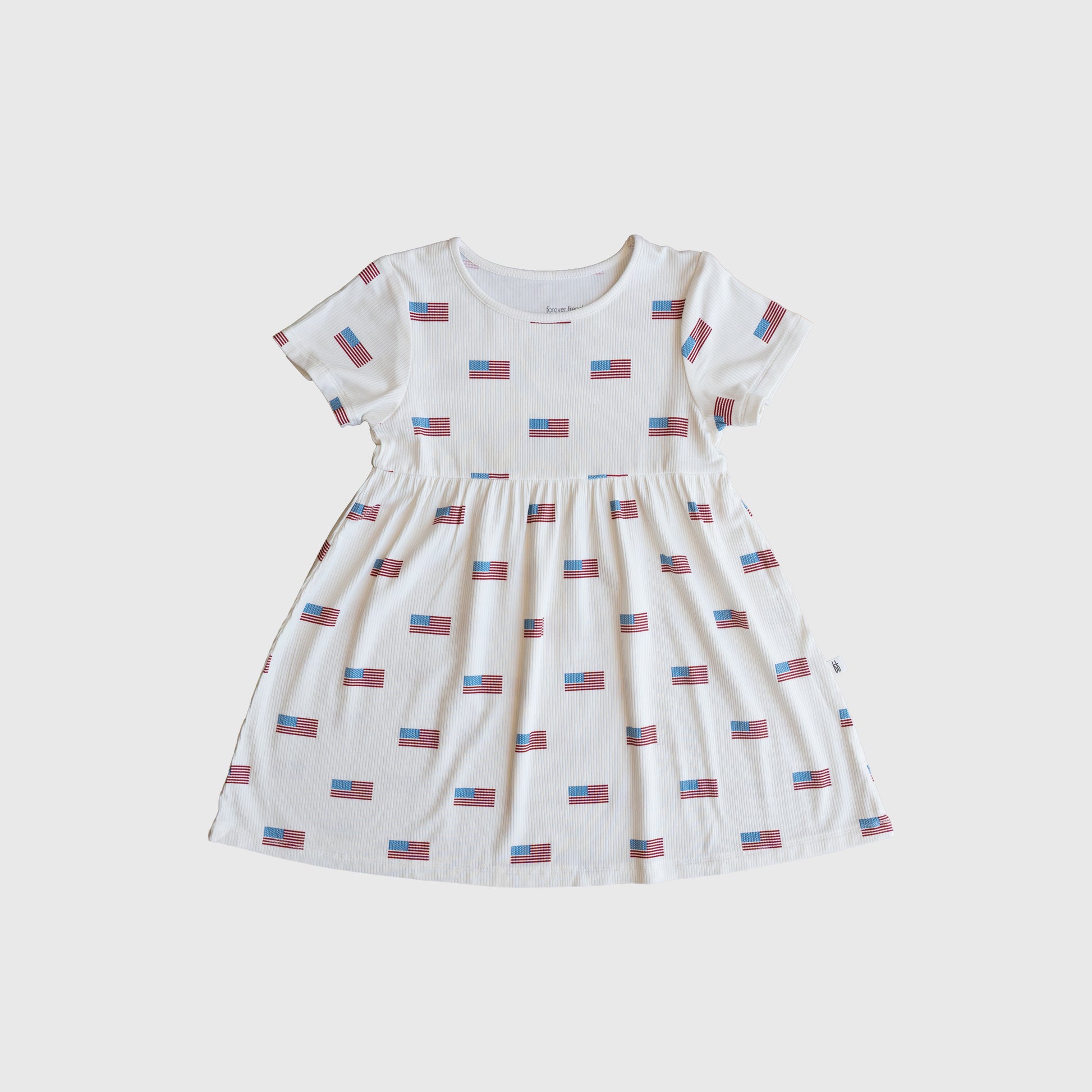 The forever french baby Bamboo T-Shirt Dress | Americana Ribbed is a hypo-allergenic, short-sleeved white children’s dress with a round neck, gathered waist, and small American flag print for softness and patriotic style.