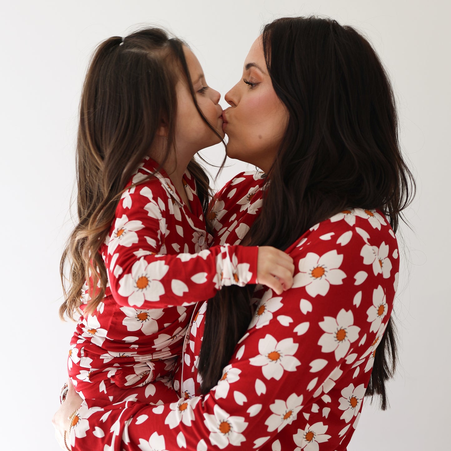 A woman and a young girl share a kiss, dressed in matching forever french baby Girl's Bamboo Button Up Lounge Sets in Cherry Blossoms print, against a white background.