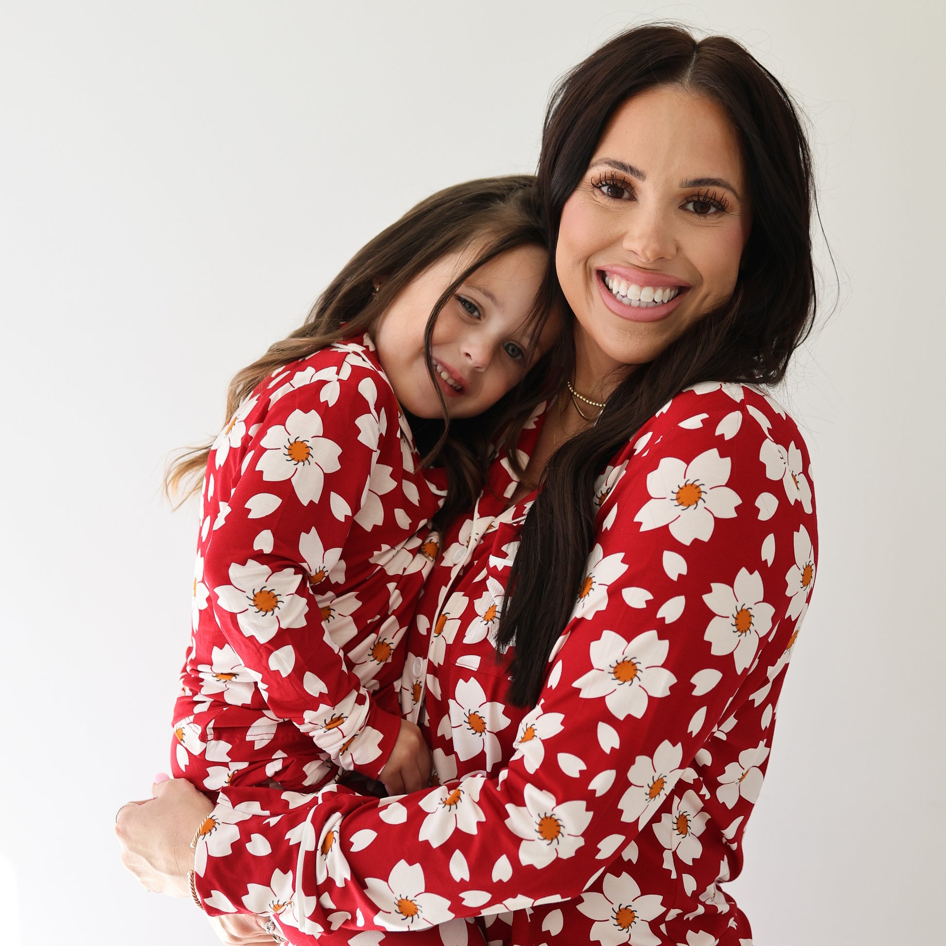 A woman holds a young girl, both smiling and posing in forever french baby’s Girl's Bamboo Button Up Lounge Set in Cherry Blossoms, against a plain white background.