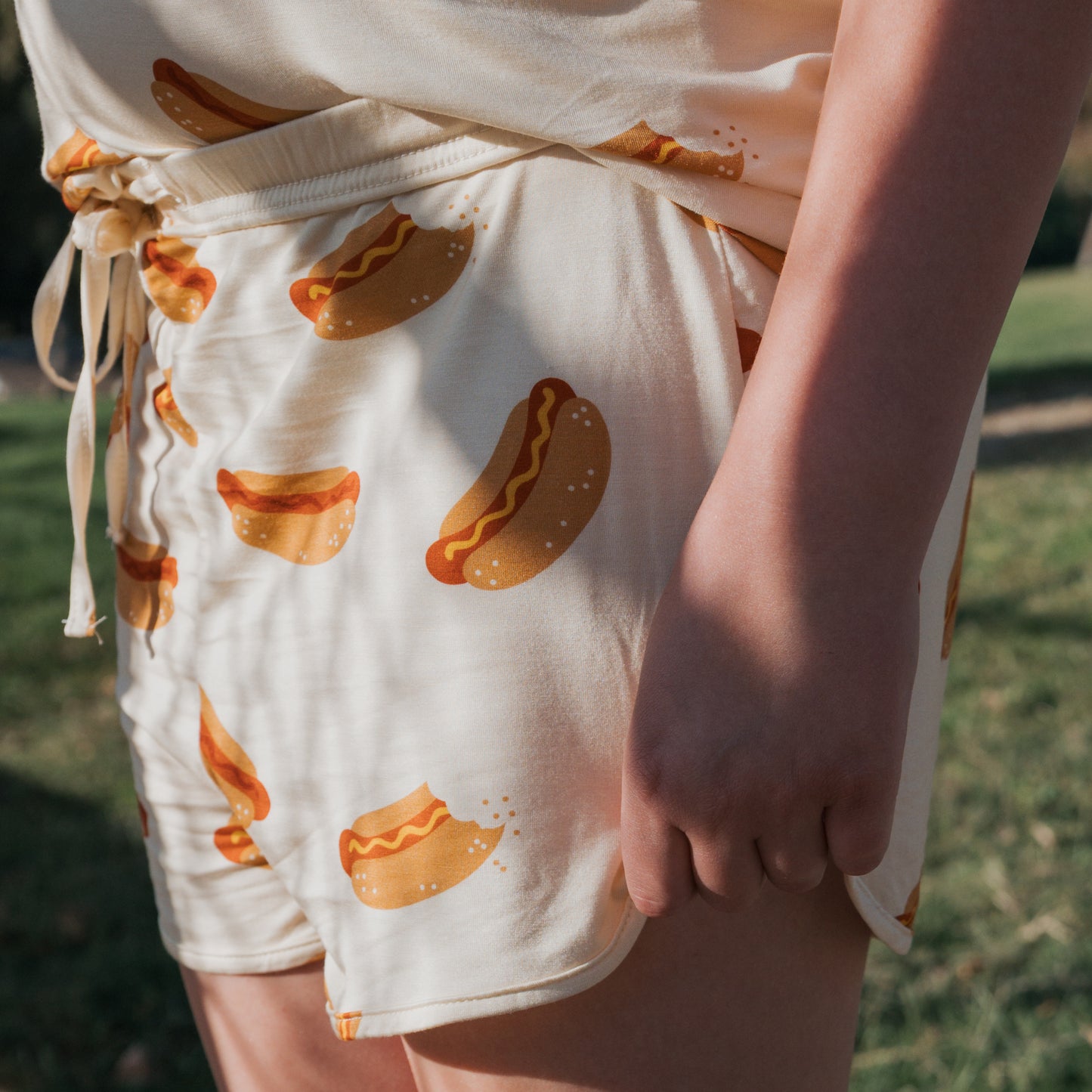 A girl enjoys the outdoors in sunlight, wearing the hypo-allergenic forever french baby Girl's Bamboo Short Set | Hot Dogs—featuring a playful hot dog print and crafted in cream for comfort.