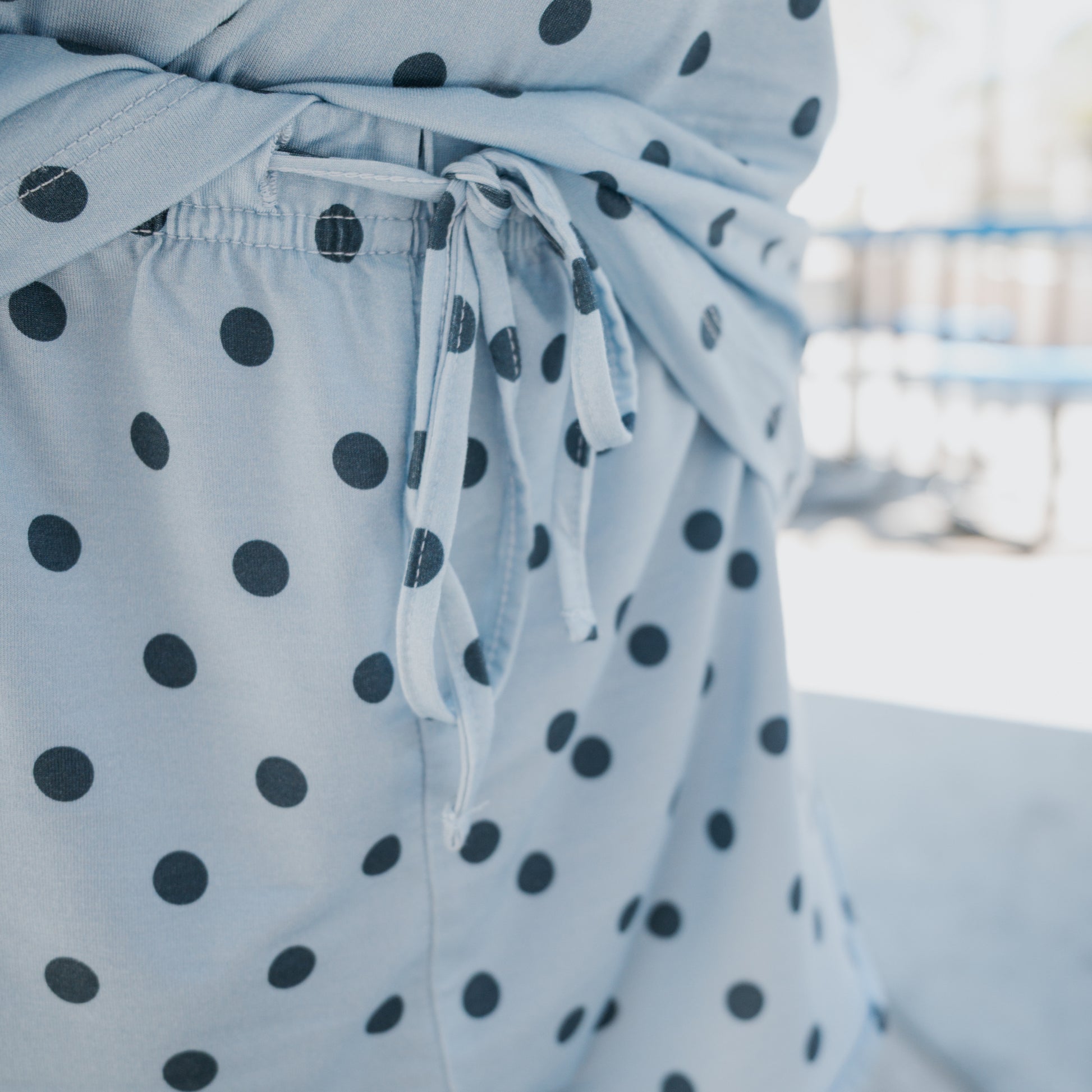 Close-up of a light blue, breathable fabric with black polka dots, featuring a tied waistband and seam details—part of the Girl's Bamboo Short Set | Sully by forever french baby. Made from hypo-allergenic bamboo textile, this set offers both comfort and style. Background is blurred and outdoors.