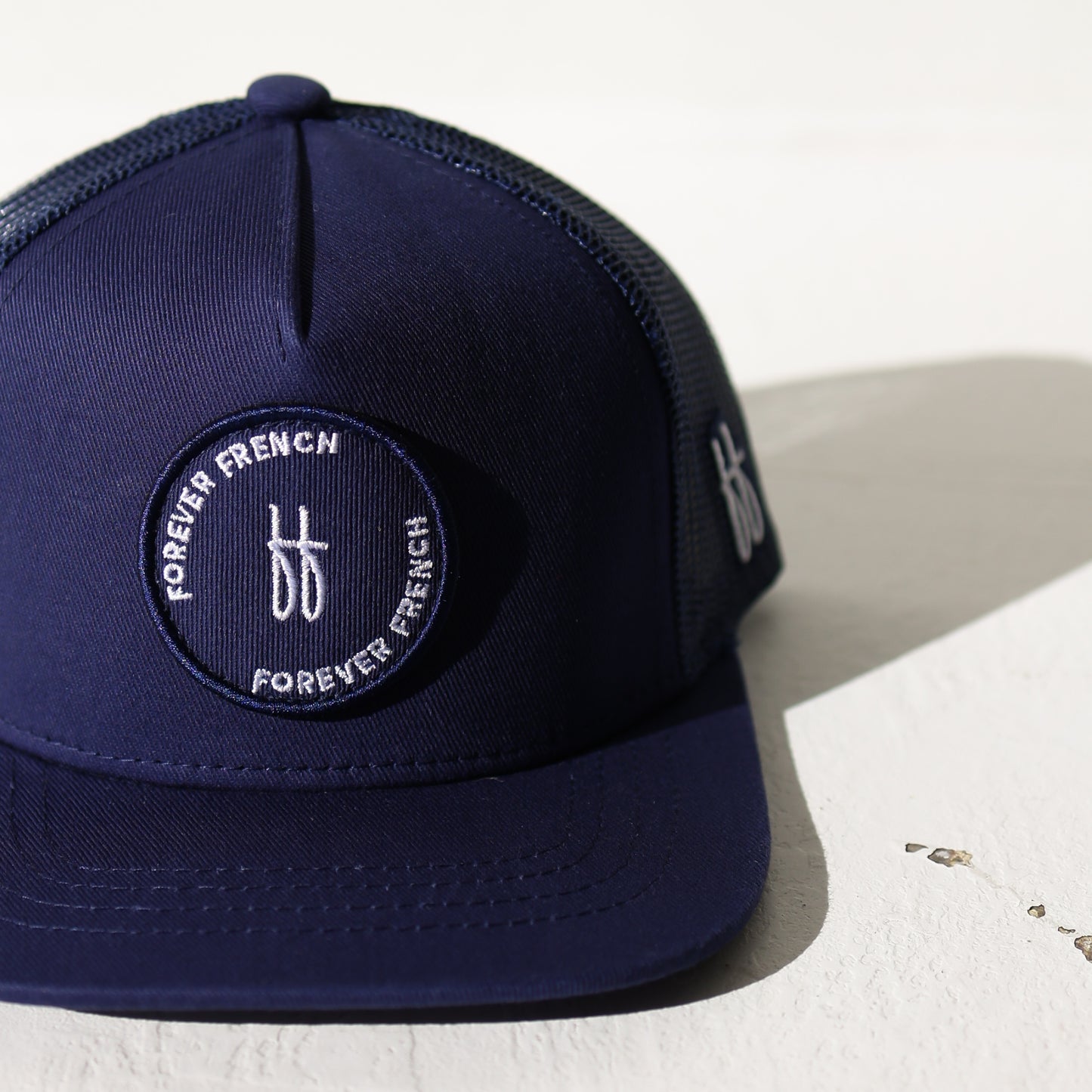 The Snapback | Blue by forever french baby is a navy trucker hat with a mesh back, a "FOREVER FRENCH" circular patch with "ff" embroidered in the center, and the forever french baby "ff" logo on the right side.