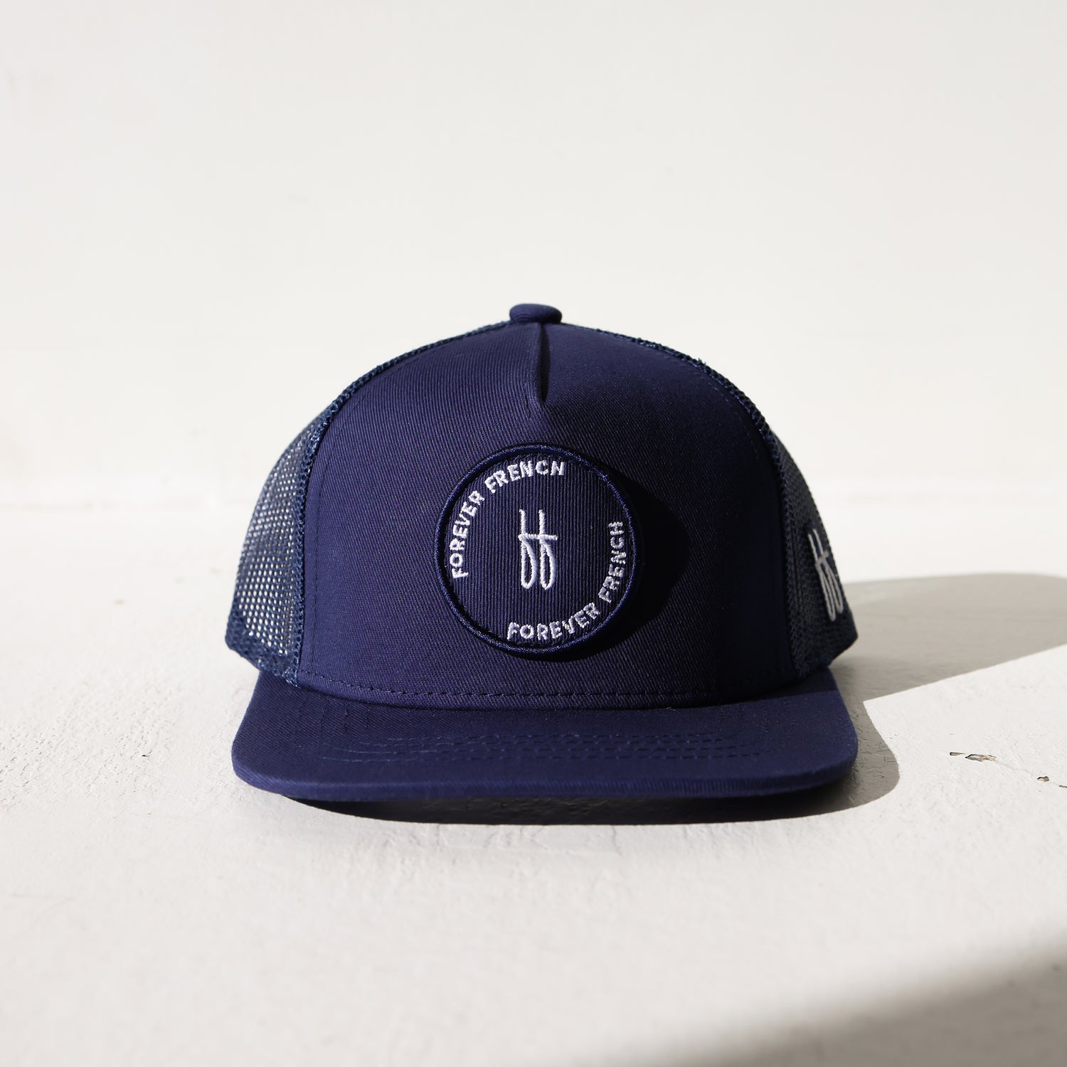 The Snapback | Blue by forever french baby is a navy mesh-back trucker hat with a circular patch featuring "FOREVER FRENCH" text and a white "ff" logo—ideal as a stylish forever french baby accessory.