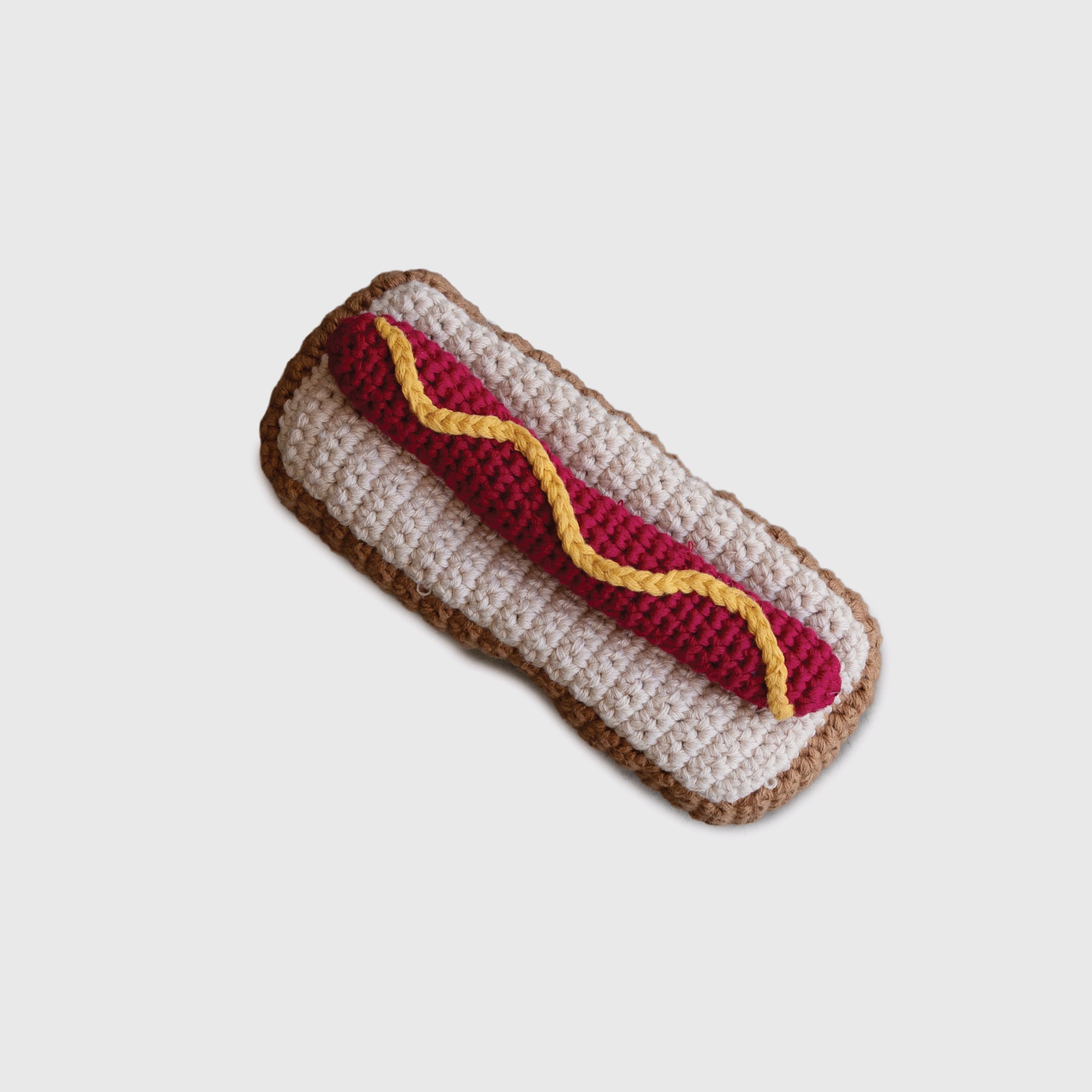 The *SHIPS IN 1 WEEK* Knit Rattle | Hot Dog by forever french baby features a tan bun, red sausage, and yellow mustard—all crafted from yarn. This cute summer baby toy is shown on a plain white background.