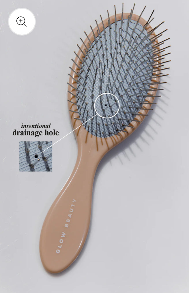 The Glow Beauty Hair Brush by forever french baby, featuring a beige design and labeled "GLOW BEAUTY", includes a rectangular drainage hole in the center of its bristle pad for easy cleaning. The thin, evenly spread bristles make it an excellent Detangling Brush. An annotation highlights the intentional drainage hole for added convenience.