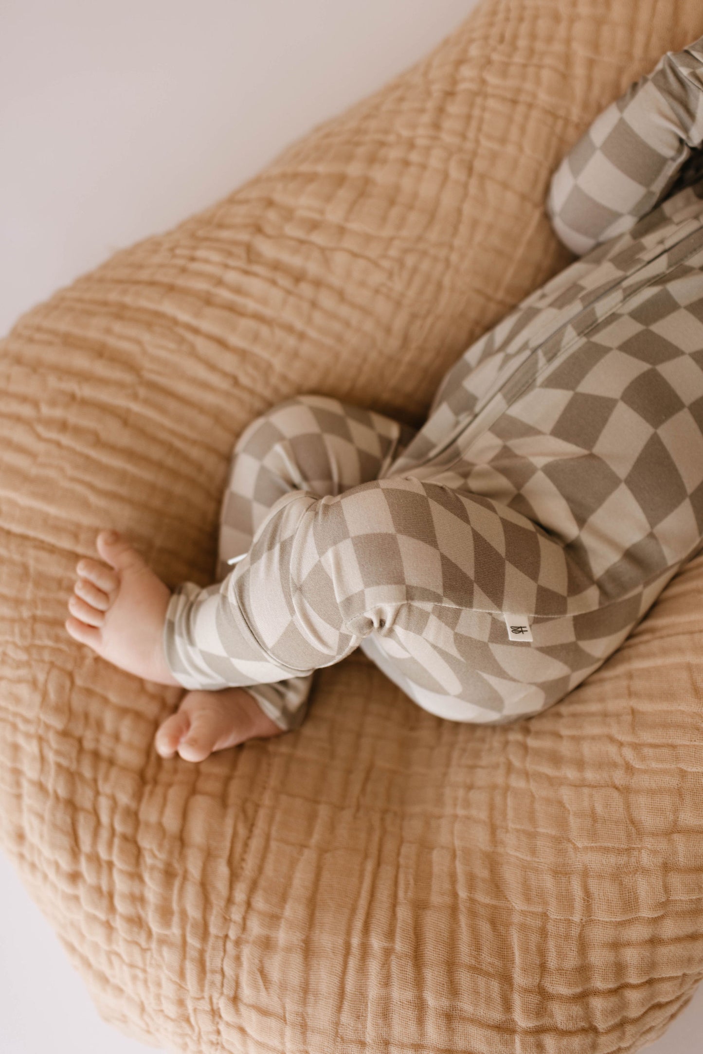 A baby in gray and white patterned pajamas lies on the ultra-soft Latte Quilt by forever french baby. The baby's legs are crossed, drawing attention to the lower half of their body and feet, perfectly showcasing the charm of Forever French Baby elegance.