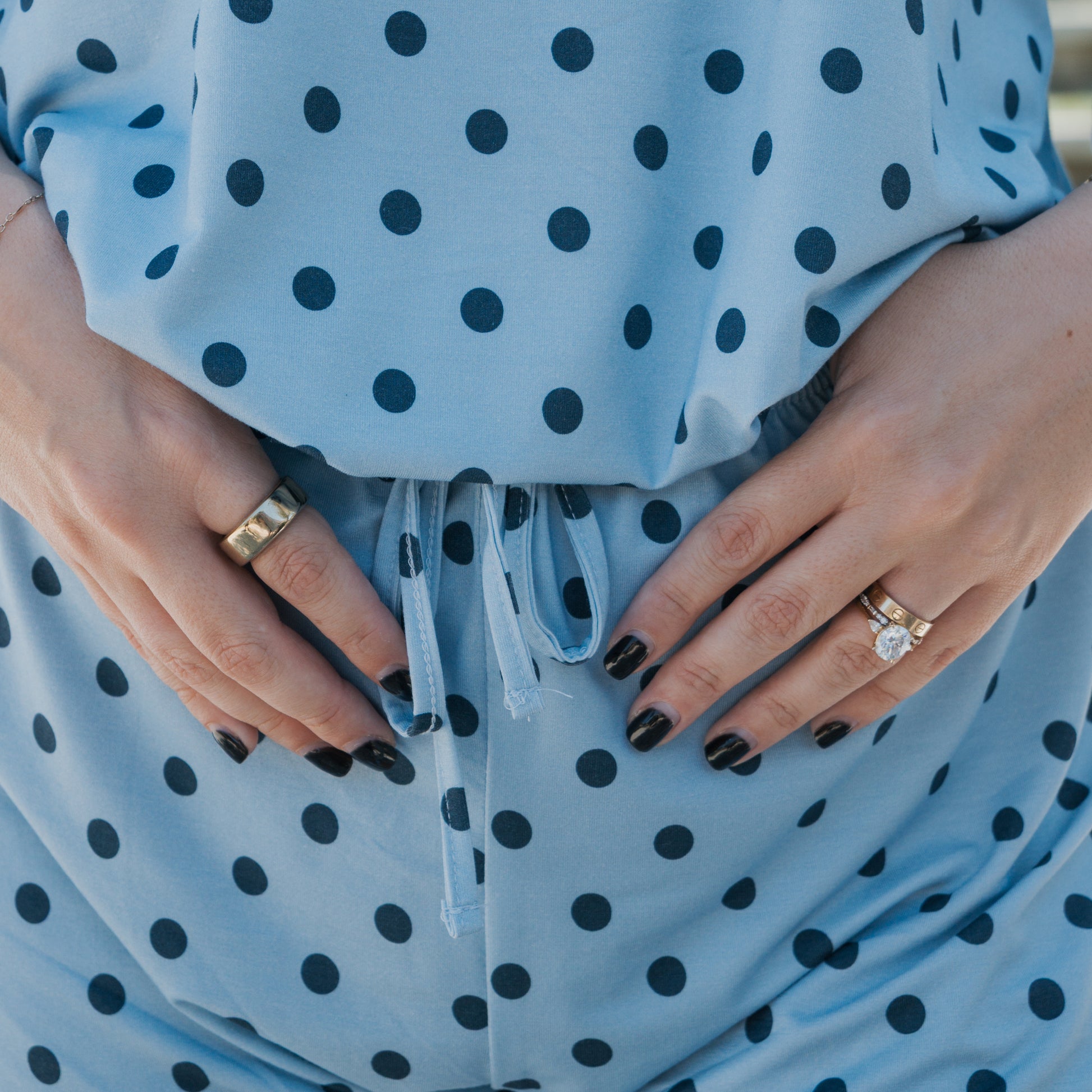 Close-up of hands with black nail polish and rings resting on a baby bump, featuring the Women's Bamboo Short Set | Sully by forever french baby — a soft, stylish, and hypo-allergenic blue polka dot pajama set.