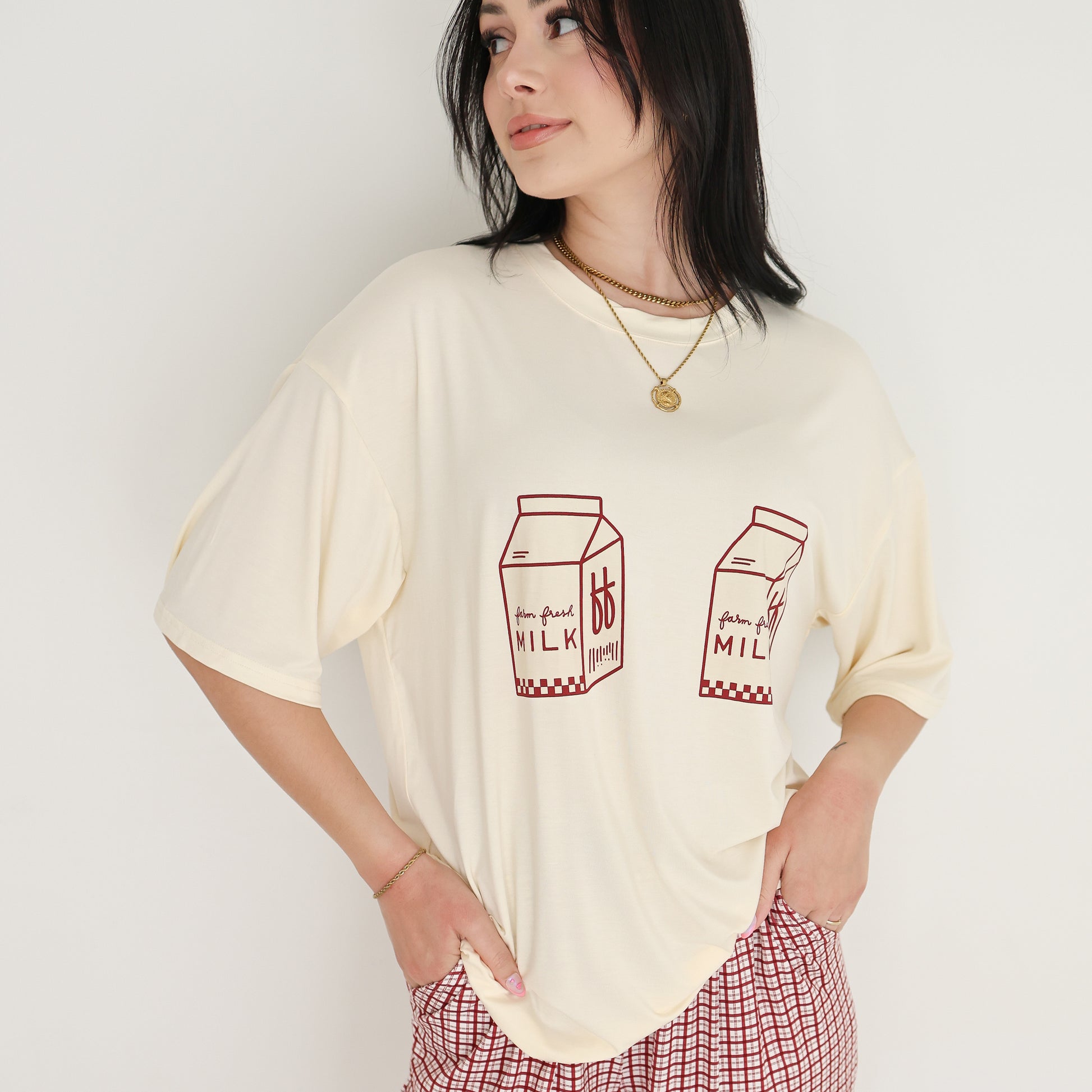 A woman poses with one hand on her hip against a white background, wearing the forever french baby Short Sleeve Women's Bamboo Lounge Set | Milk & Window Pane, featuring red milk carton graphics and red checkered pants.