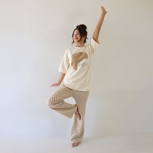 A woman balances in tree pose, wearing the forever french baby Women's Knit Pant Set | Croissants, with one arm raised and the other relaxed by her side, set against a plain white background.