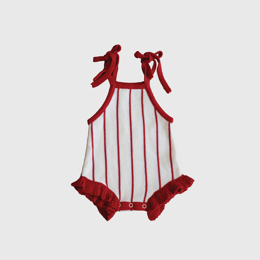 The forever french baby Knit Ruffle Romper | Picnic Pinstripe is a 100% cotton baby romper with red shoulder tie straps, red trim, vertical red stripes on white, ruffled leg openings, and crotch snap buttons.