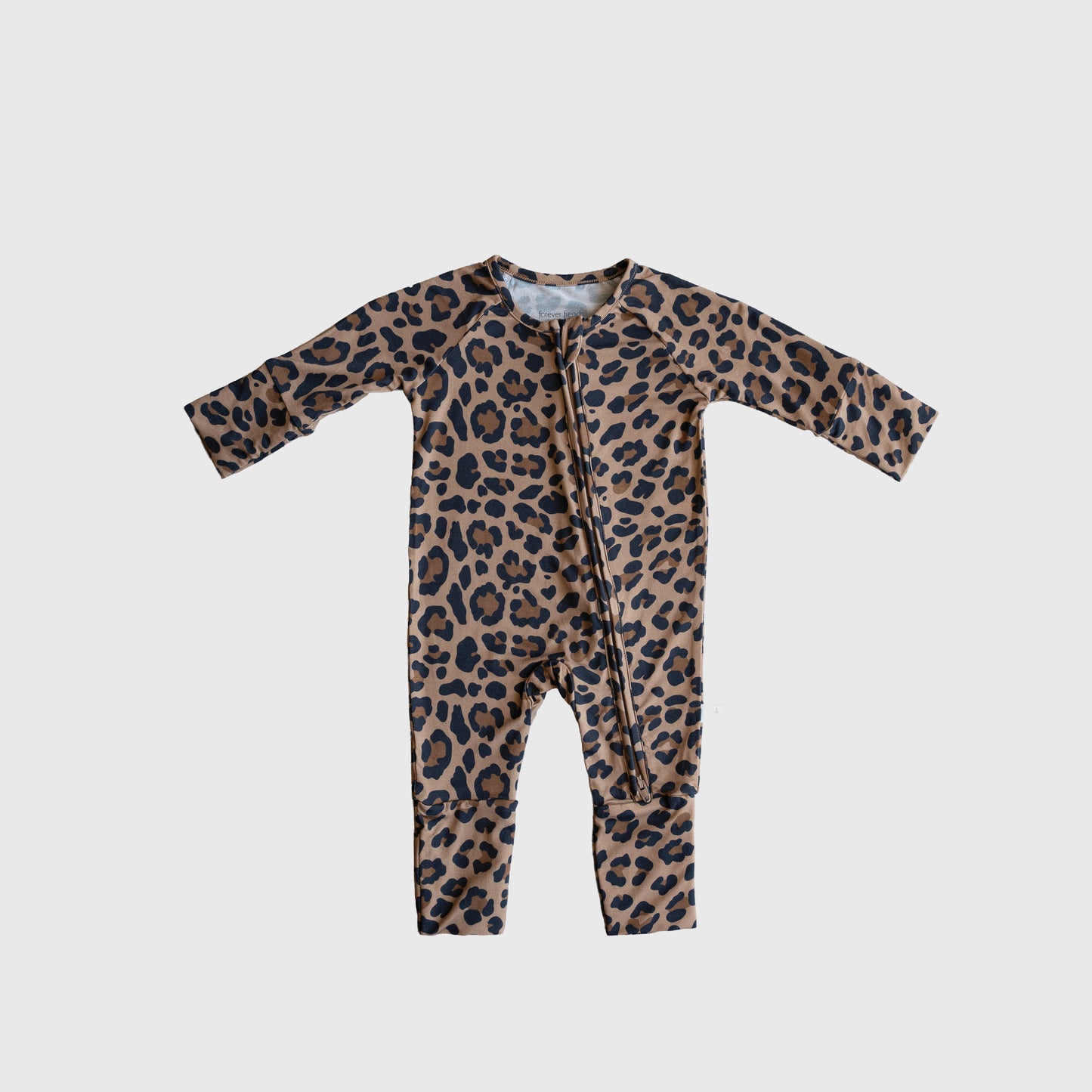 The Bamboo Zip Pajamas | Leopard by forever french baby are long-sleeve, long-leg baby pajamas in a brown and black leopard print, made from breathable fabric with a diagonal zipper. They're shown laid flat on a plain white background.