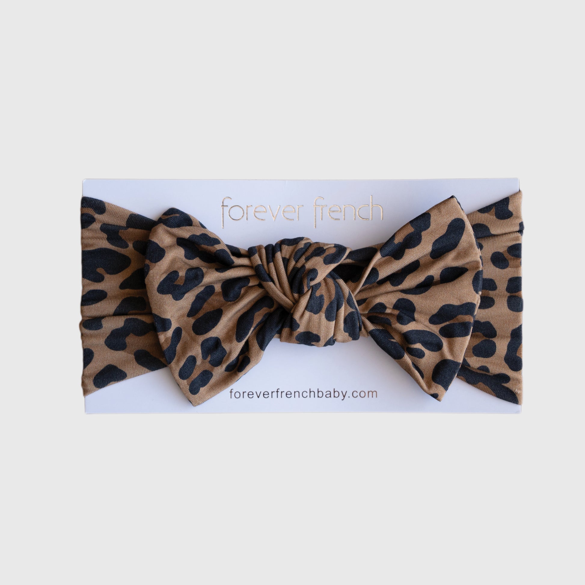 A Bamboo Head Wrap | Leopard by forever french baby, featuring a brown leopard print with black spots and a large bow, is displayed on white packaging labeled "forever french baby" and "foreverfrenchbaby.com".