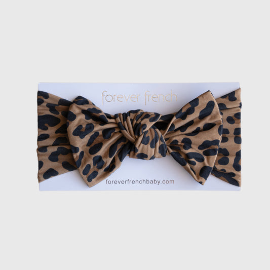 A Bamboo Head Wrap | Leopard by forever french baby, featuring a brown leopard print with black spots and a large bow, is displayed on white packaging labeled "forever french baby" and "foreverfrenchbaby.com".