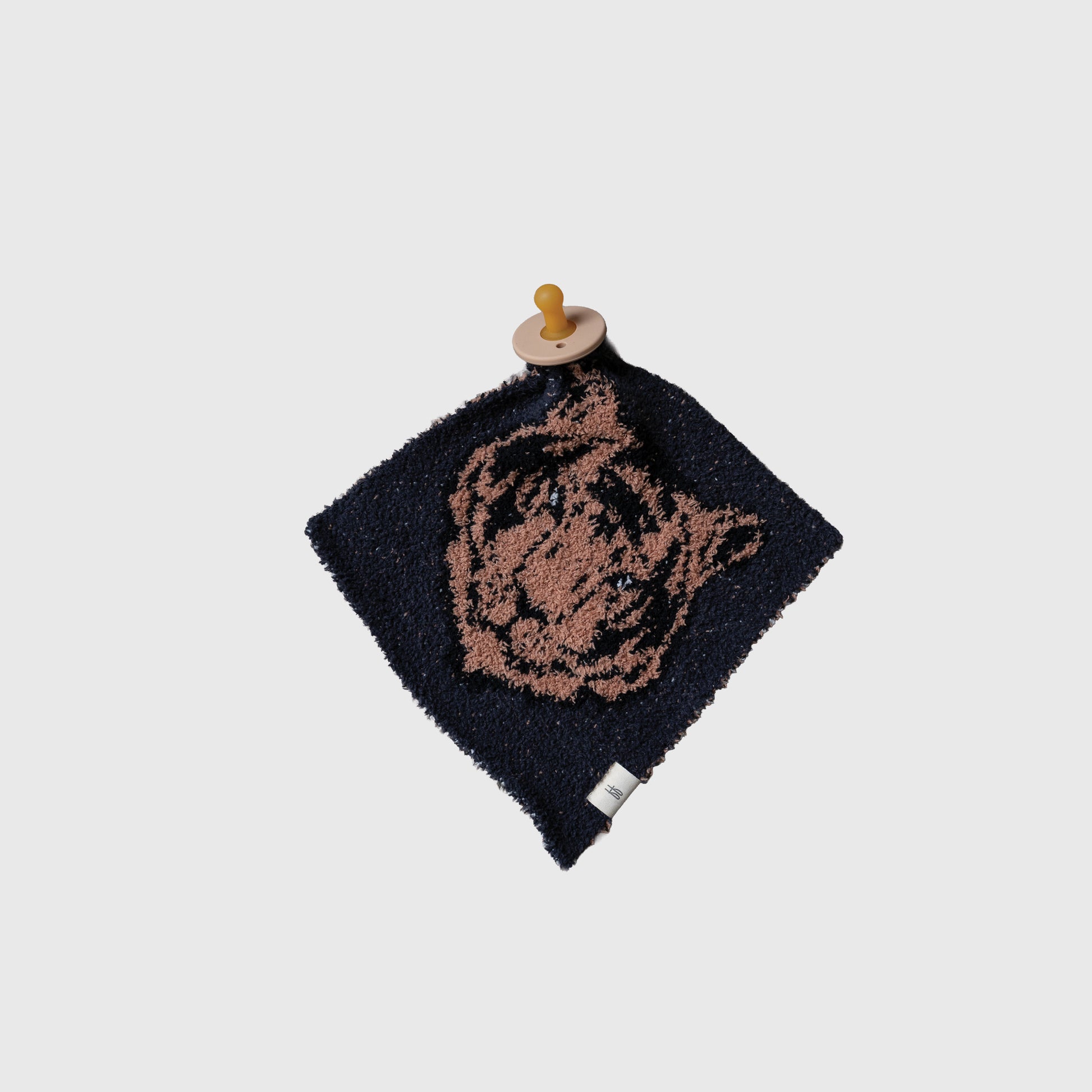 The “Lovey | Tiger” by forever french baby is a square navy blue microfiber blanket with a brown tiger face, attached to a wooden pacifier and finished with a small white fabric tag in one corner.