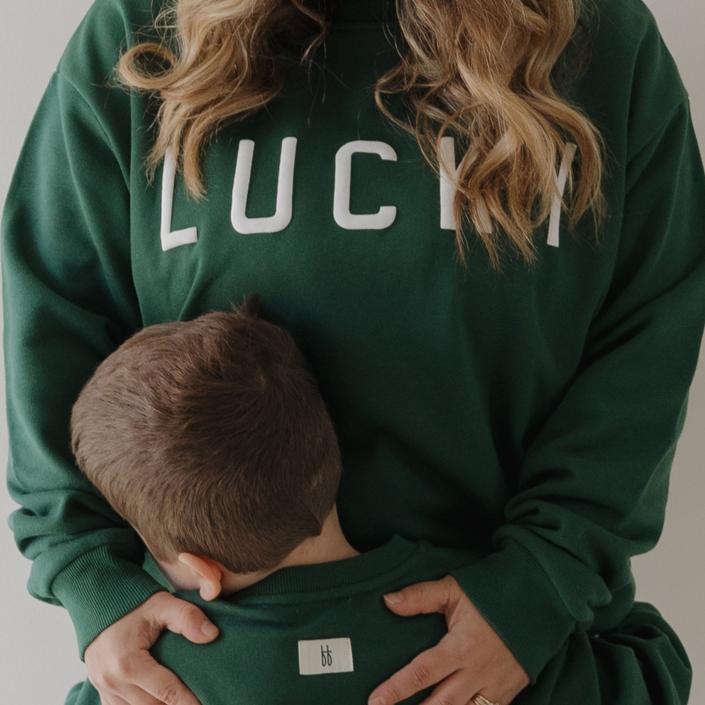 A woman wears the forever french baby Adult Sweatshirt | Lucky in green as she hugs a young boy, both dressed in matching green tops—capturing warmth and comfort, perfect inspiration for family sweatshirts.
