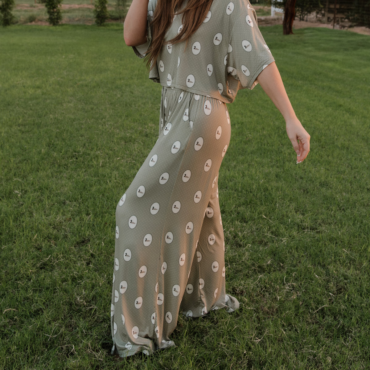 A person wearing the Women’s Bamboo Crop Tee Lounge Set by forever french baby in the Mallard Frames print walks on grass with their back turned, one arm slightly raised.