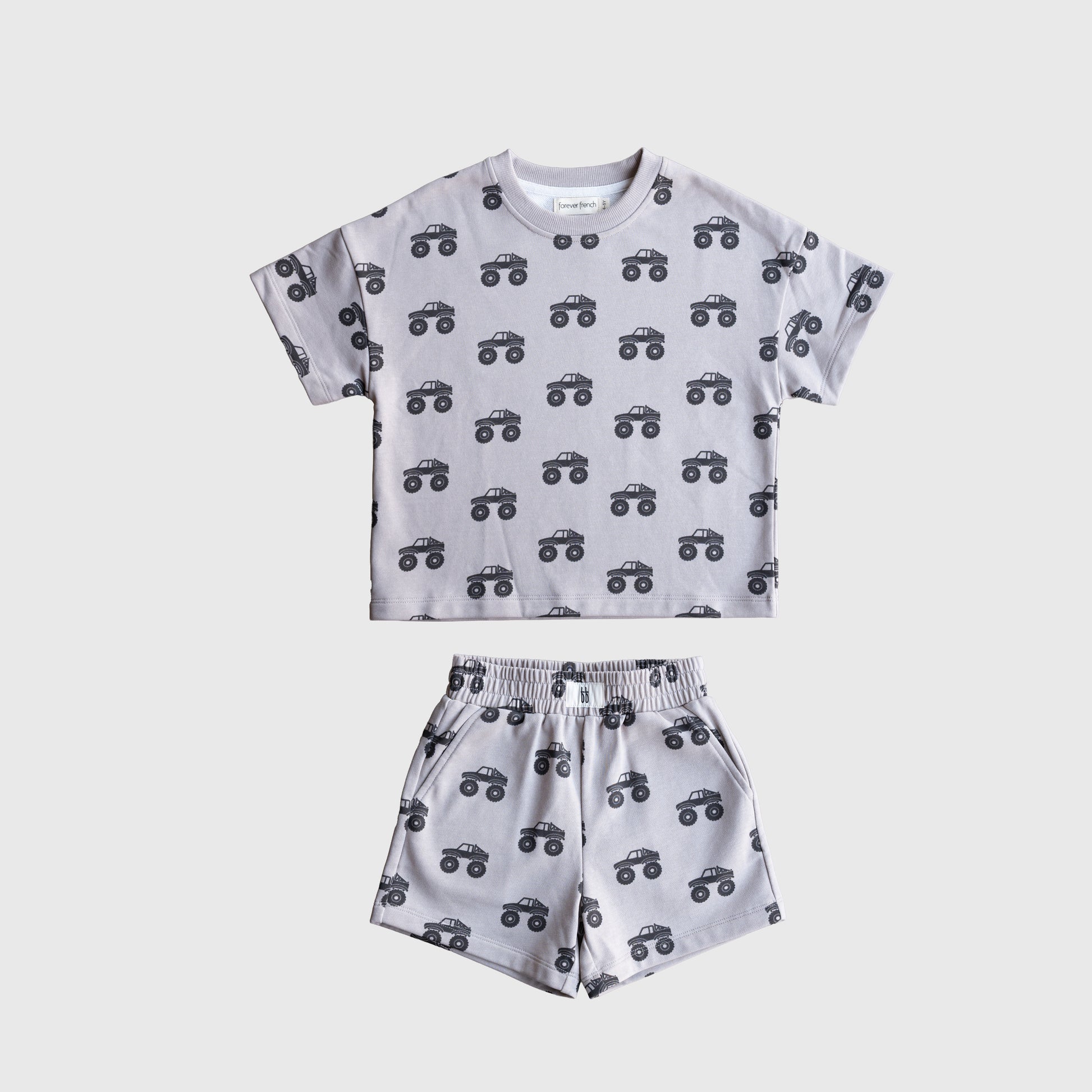 The forever french baby French Terry Short Set | Monster Truck is a kids’ outfit with a short sleeve top and shorts in light gray, featuring black cartoon monster trucks, shown flat on a white background.