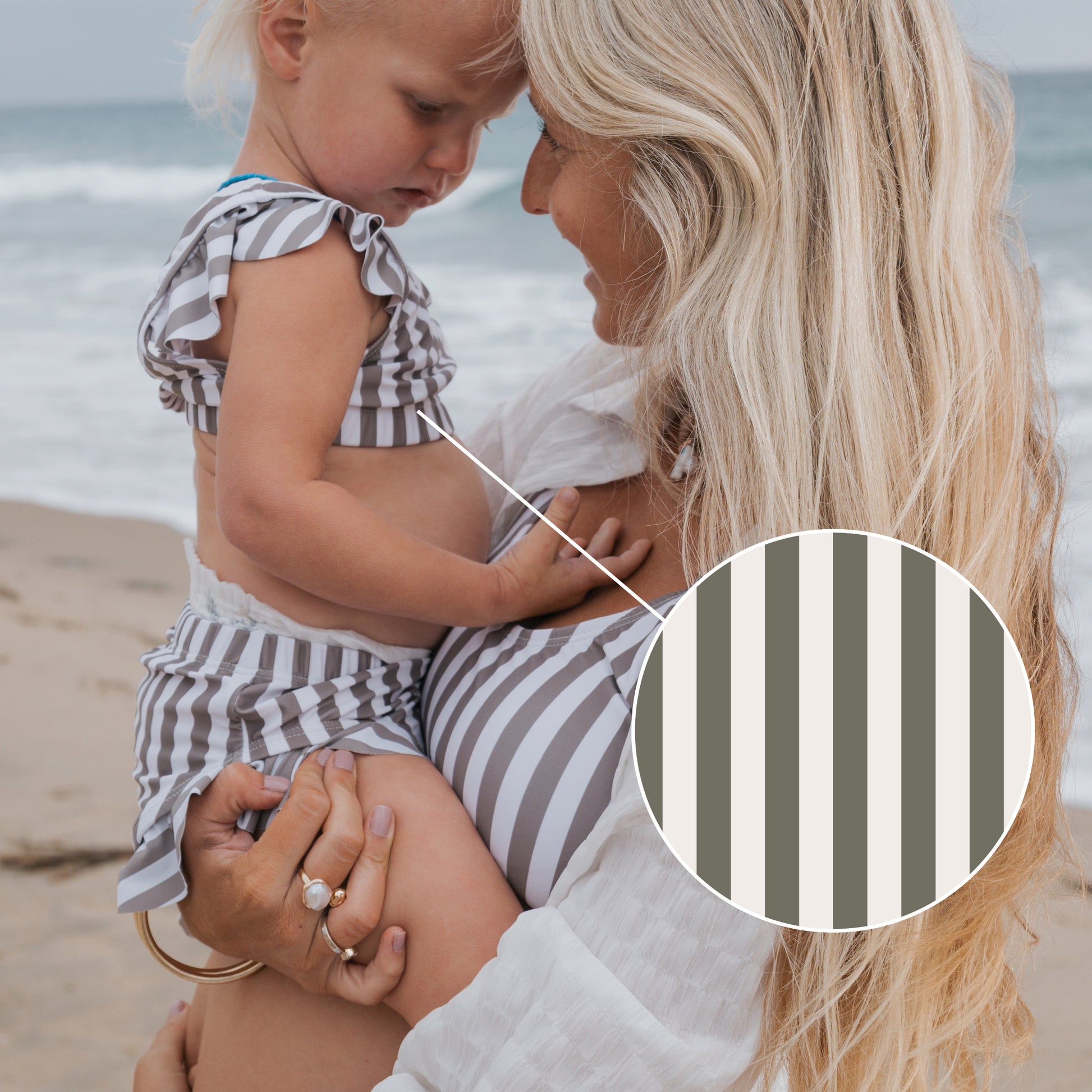 A woman holds a young child on the beach, both in matching forever french baby outfits. A circular inset highlights the "Girl's Two Piece Swimsuit | Olive Stripe" pattern as the ocean stretches out behind them.