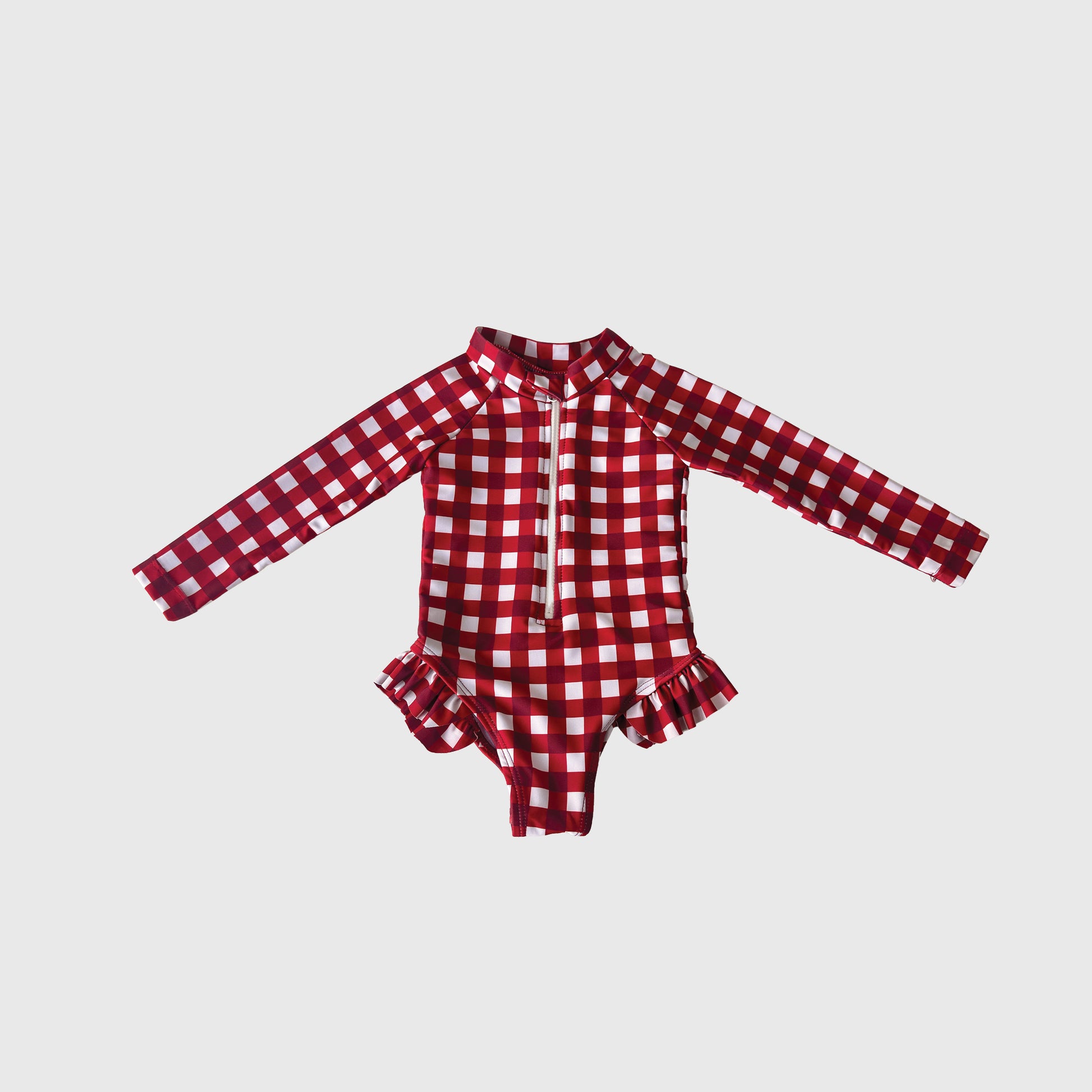 The Girl's Long Sleeve Swimsuit in Scarlet Gingham from forever french baby features a red and white plaid print, front zipper, and ruffle hip details—perfect summer swimwear, shown on a plain white background.