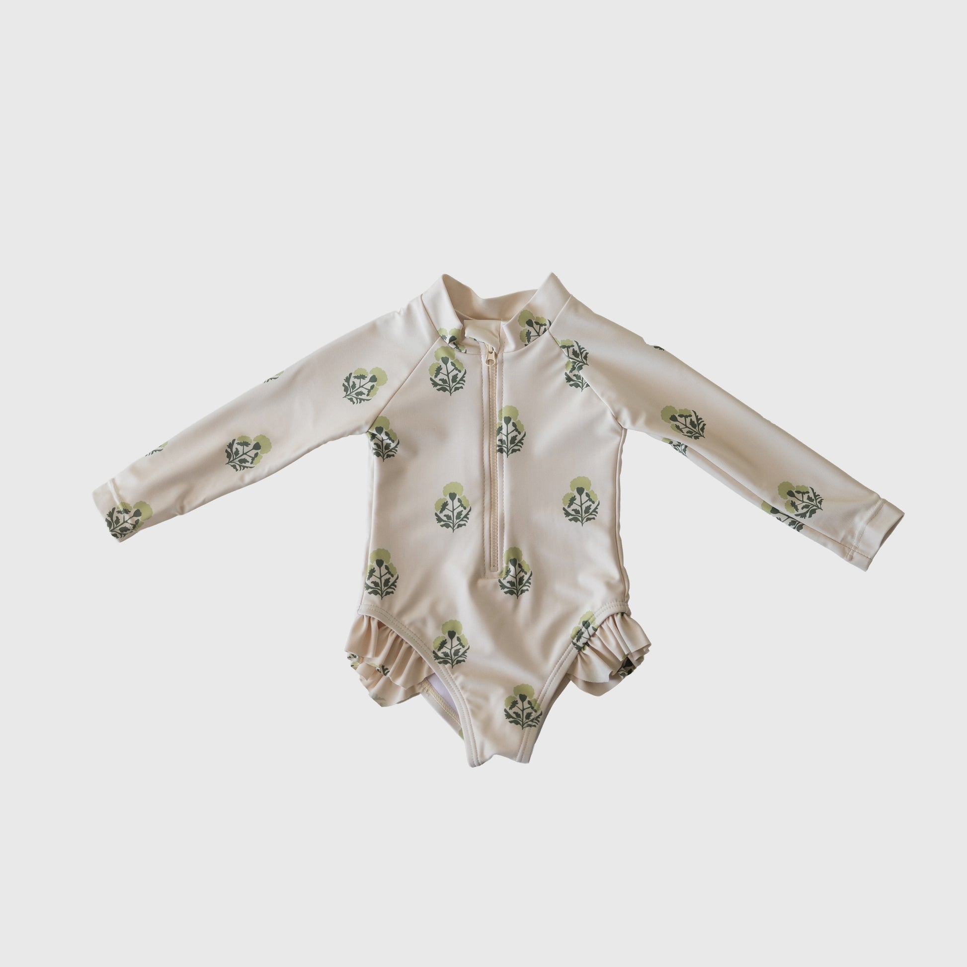 The Girl's Long Sleeve Swimsuit | Marigold by forever french baby features cream fabric, green leaf print, front zipper, and ruffled leg openings. This cute one piece is shown flat on a white background.