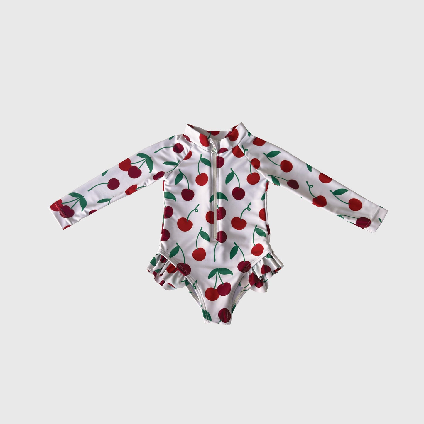 The Girl's Long Sleeve Swimsuit | Cherry by forever french baby features a cherry and green leaf print, front zipper, and hip ruffles—perfect for summer swimwear—shown on a plain white background.