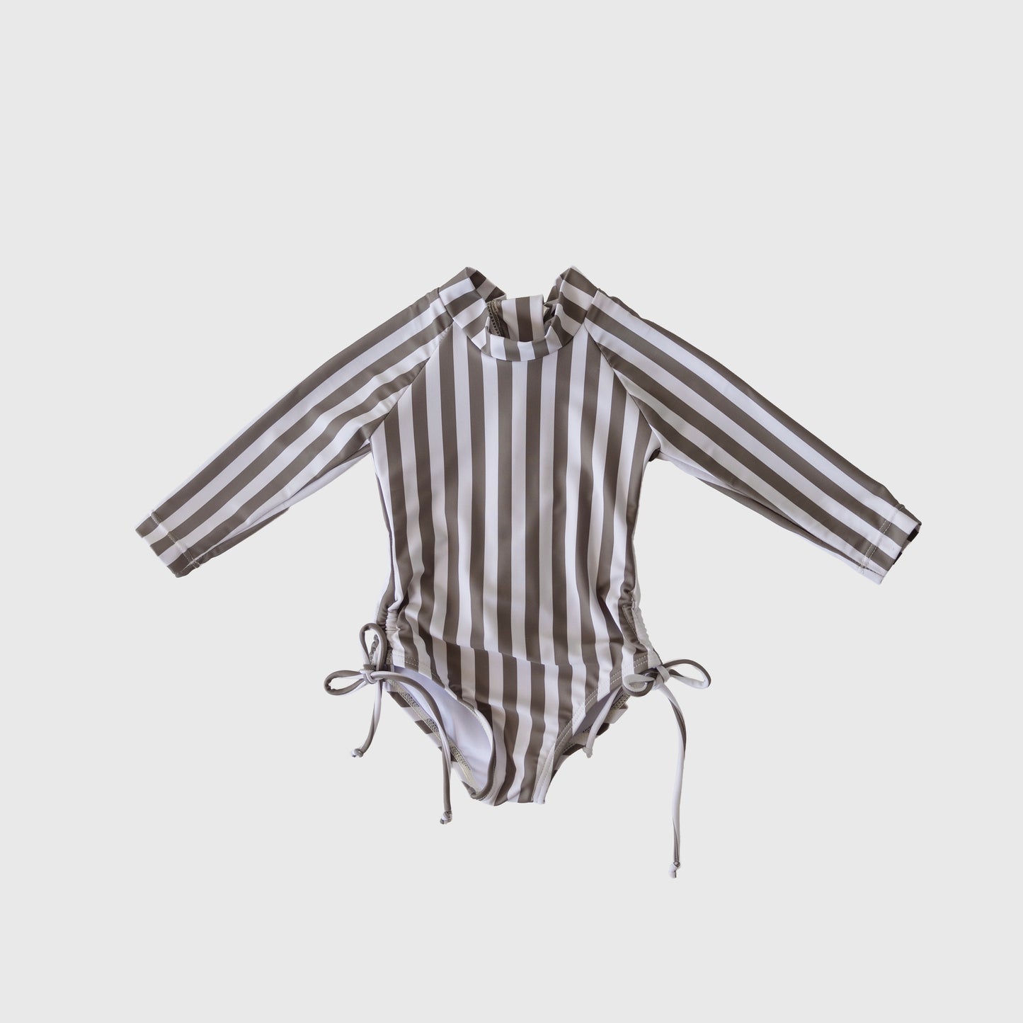 The forever french baby Girl's Long Sleeve Swimsuit in Olive Stripe features vertical olive and white stripes, a high neckline, long sleeves, and chic hip ties. This one-piece is shown against a plain white background.