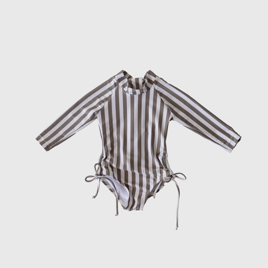 The forever french baby Girl's Long Sleeve Swimsuit in Olive Stripe features vertical olive and white stripes, a high neckline, long sleeves, and chic hip ties. This one-piece is shown against a plain white background.