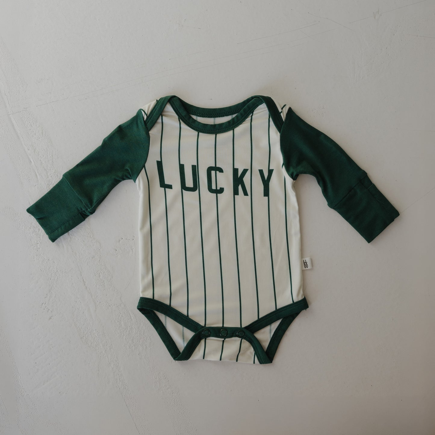 The forever french baby Long Sleeve Bamboo Snapsuit | Lucky features green long sleeves, vertical stripes, and "LUCKY" in bold green across the chest. This breathable bamboo snapsuit is shown laid flat on a light surface.