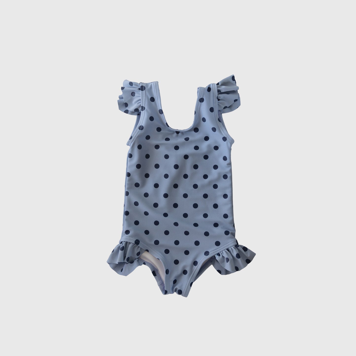 The forever French baby Girl's Sleeveless Swimsuit | Sully features light blue fabric with dark blue polka dots, ruffle shoulder straps, and leg ruffles—ideal for matching family swim. Shown on a plain white background.