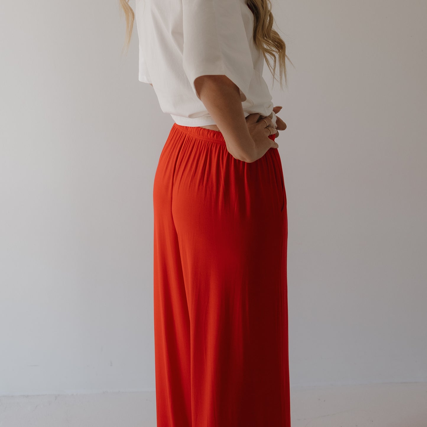 A person stands sideways with hands on hips, wearing a white tee and forever french baby Women's Bamboo Wide Leg Pants in Cherry Red, made from breathable fabric, set against a plain light background.