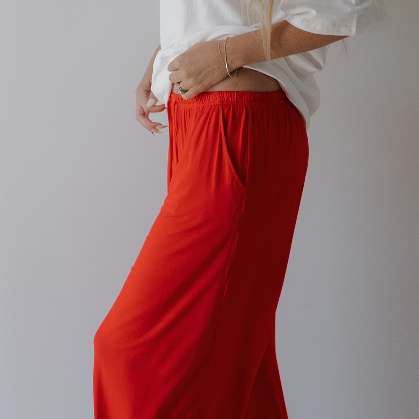 A person models forever french baby's Women's Bamboo Wide Leg Pants in Cherry Red, pairing them with a loose white top and standing against a plain light background, one hand on their hip and the other relaxed by their side.