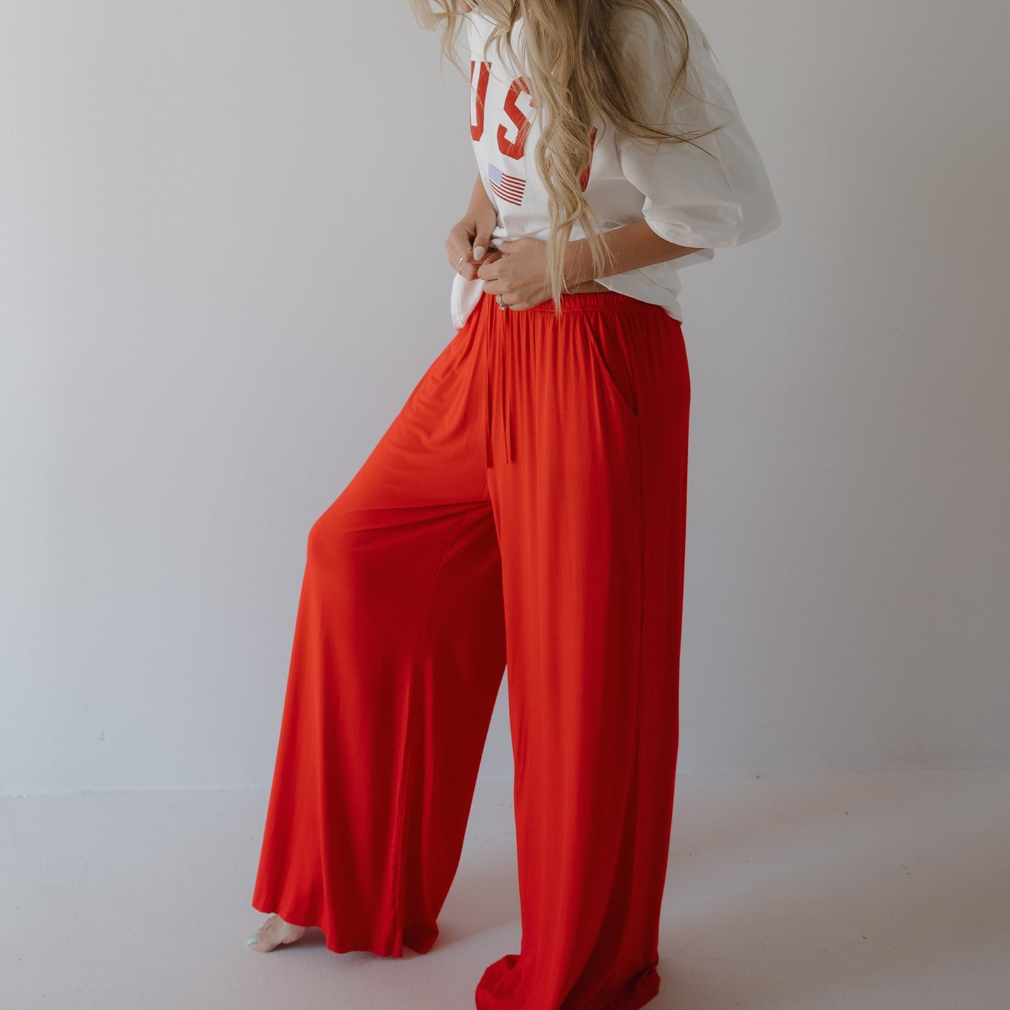 A person with long, wavy hair models forever french baby’s Women’s Bamboo Wide Leg Pants in Cherry Red and a loose white tee with “USA” in red letters, standing against a plain white background. Their face is not visible.