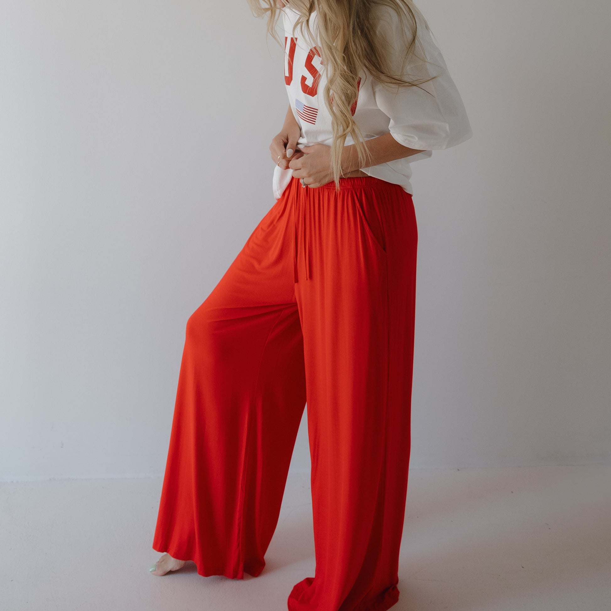 A person with long, wavy hair models forever french baby’s Women’s Bamboo Wide Leg Pants in Cherry Red and a loose white tee with “USA” in red letters, standing against a plain white background. Their face is not visible.