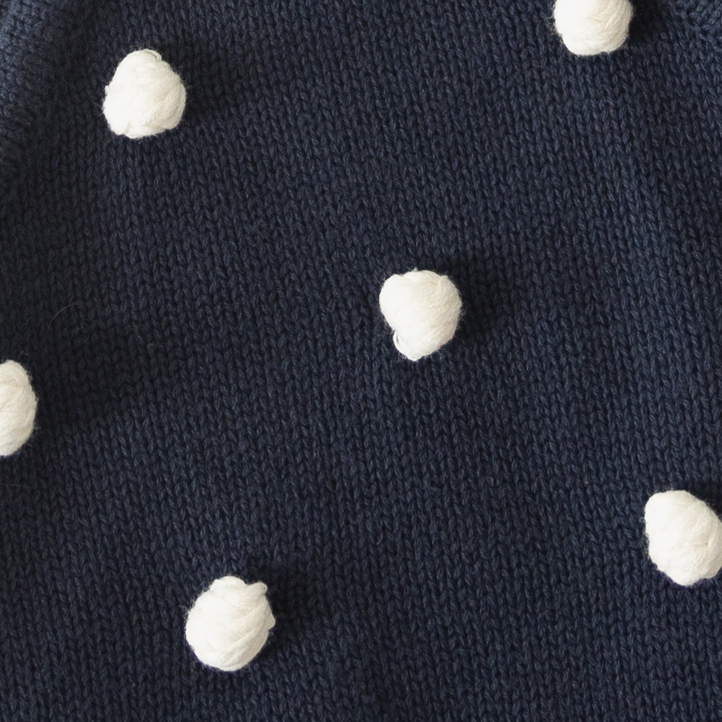 Close-up of the Knit Ruffle Romper | Emery by forever french baby in navy blue soft knit, featuring evenly spaced raised white yarn dots for a textured polka dot design.