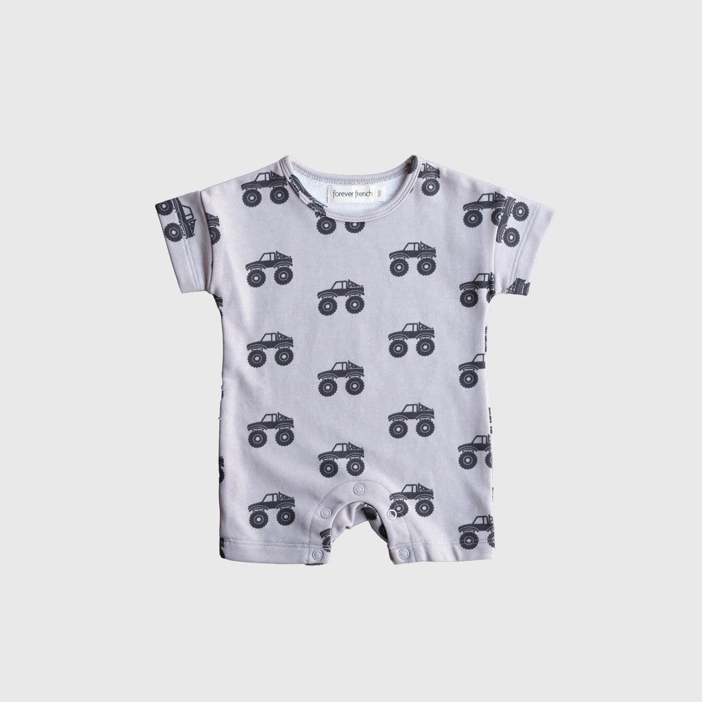 The forever french baby French Terry Romper | Monster Truck is a light gray, short-sleeve romper featuring a black monster truck print, providing breathable comfort for babies and shown flat on a white background.
