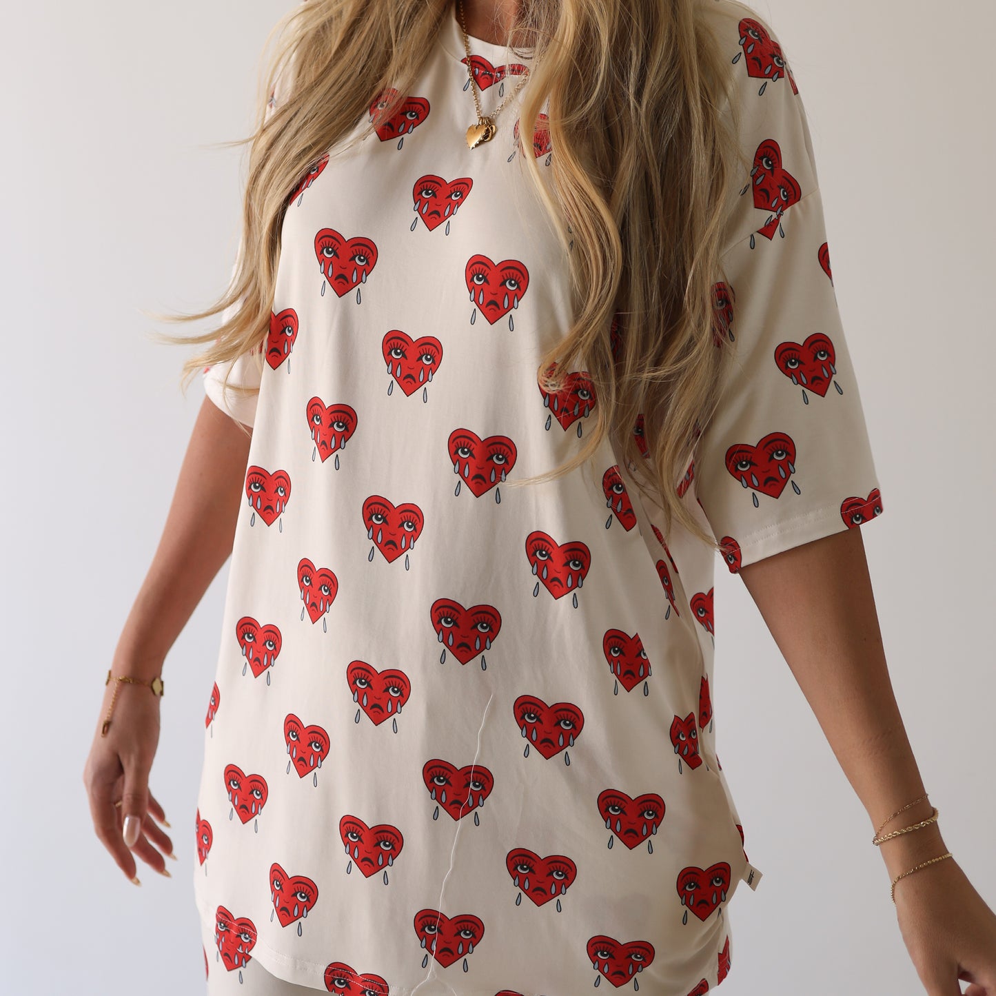 A person with long, wavy blonde hair models forever french baby’s Short Sleeve Women's Bamboo Pajamas | Sad Girl—a loose, cream top with red crying hearts—visible from shoulders to mid-thigh against a plain background.