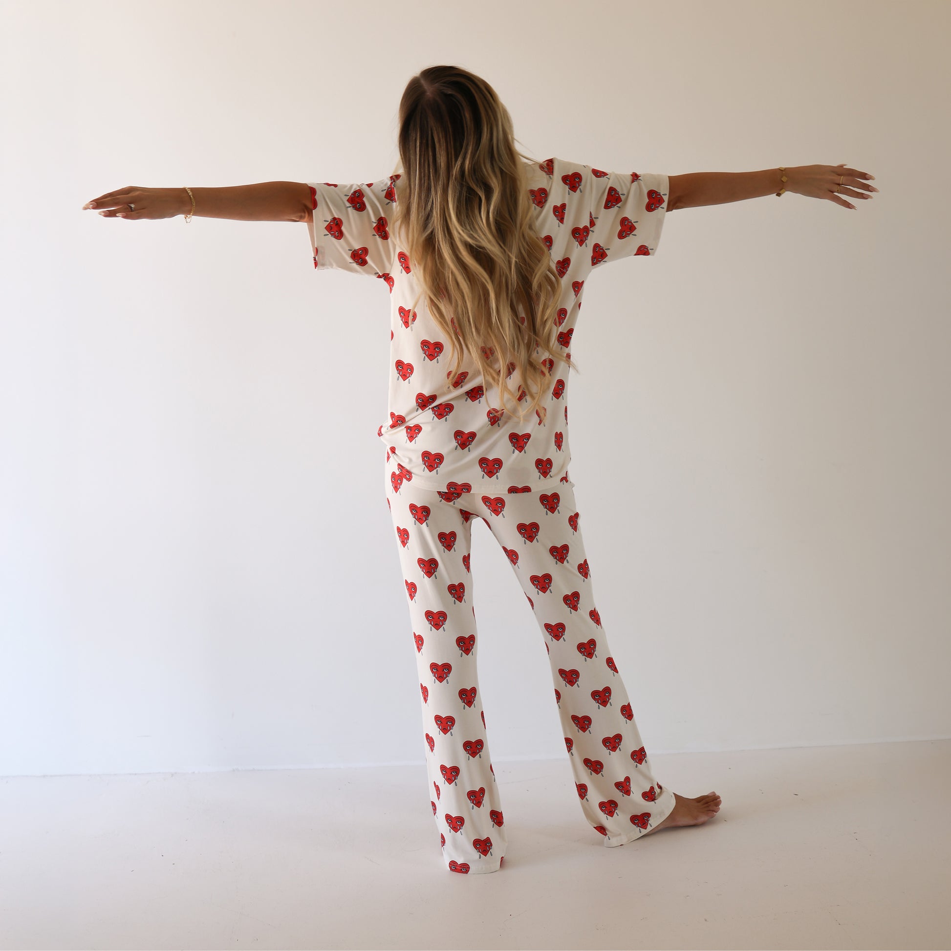 A woman with long, wavy hair stands barefoot with arms outstretched, wearing forever french baby’s Short Sleeve Women's Bamboo Pajamas | Sad Girl in a bright room—ideal for cozy, carefree mornings.