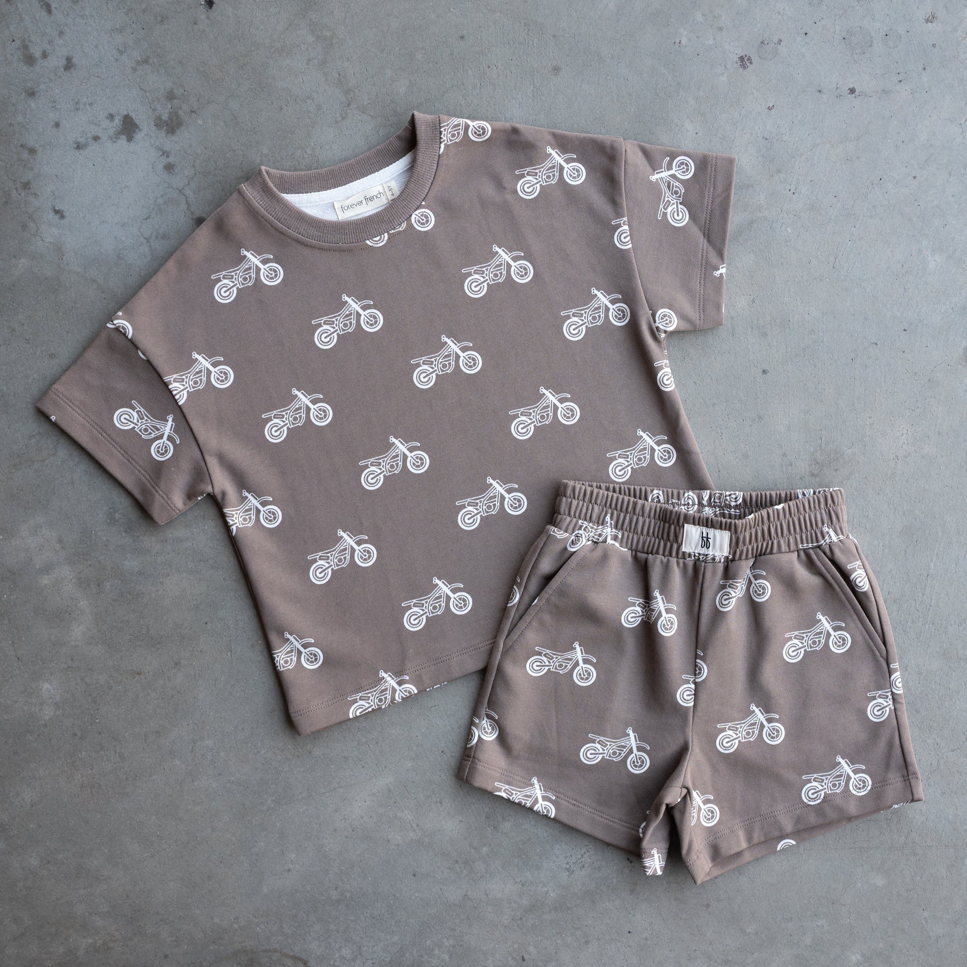 The forever french baby French Terry Short Set | Dirt Bike features a taupe short sleeve top and shorts with a white motorcycle print, shown flat on a gray concrete surface.
